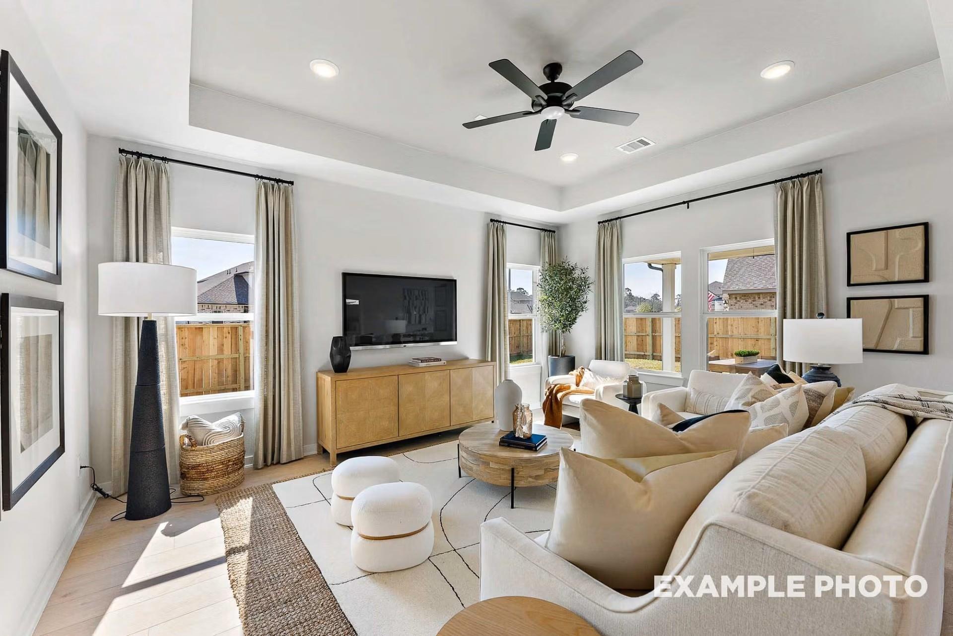 Cozy living room with white sectional sofa, mounted TV, ceiling fan, and backyard views in Davidson Homes The Everett C, Dayton, Texas