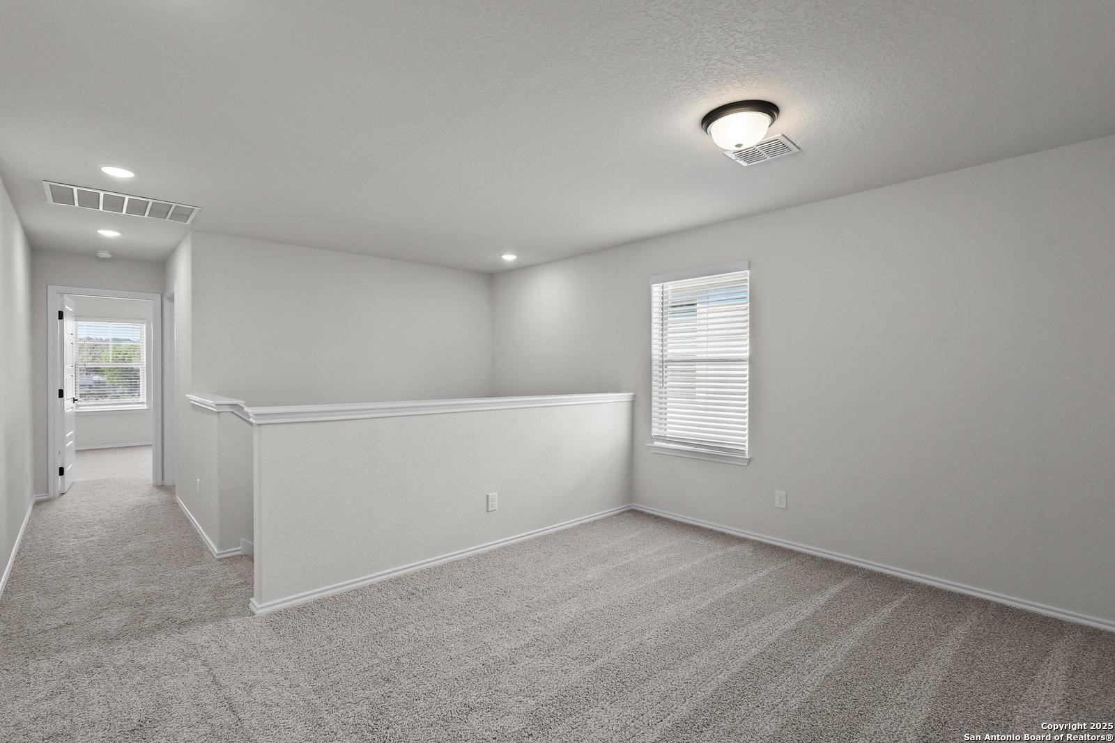 Bright upstairs hallway with light gray walls, beige carpet, white railing, and window blinds in 2-story Florence C home, San Antonio