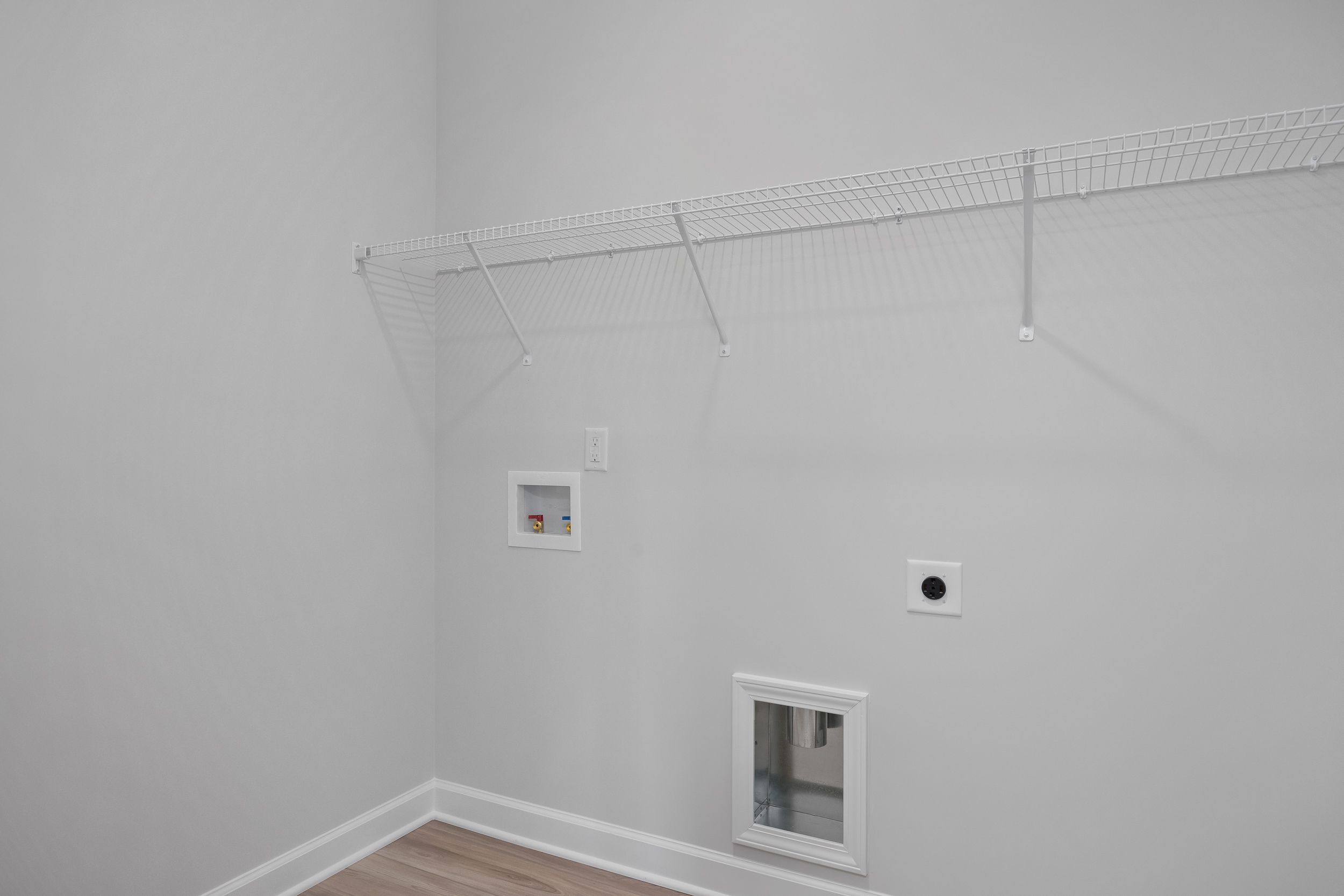 Spacious laundry room in The Daphne C with wire shelving, dryer outlet, electrical plug, and pet door on hardwood floors