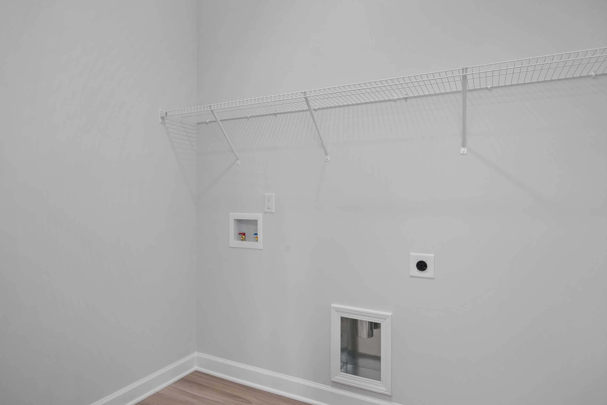 Spacious laundry room in The Daphne C with wire shelving, dryer outlet, electrical plug, and pet door on hardwood floors
