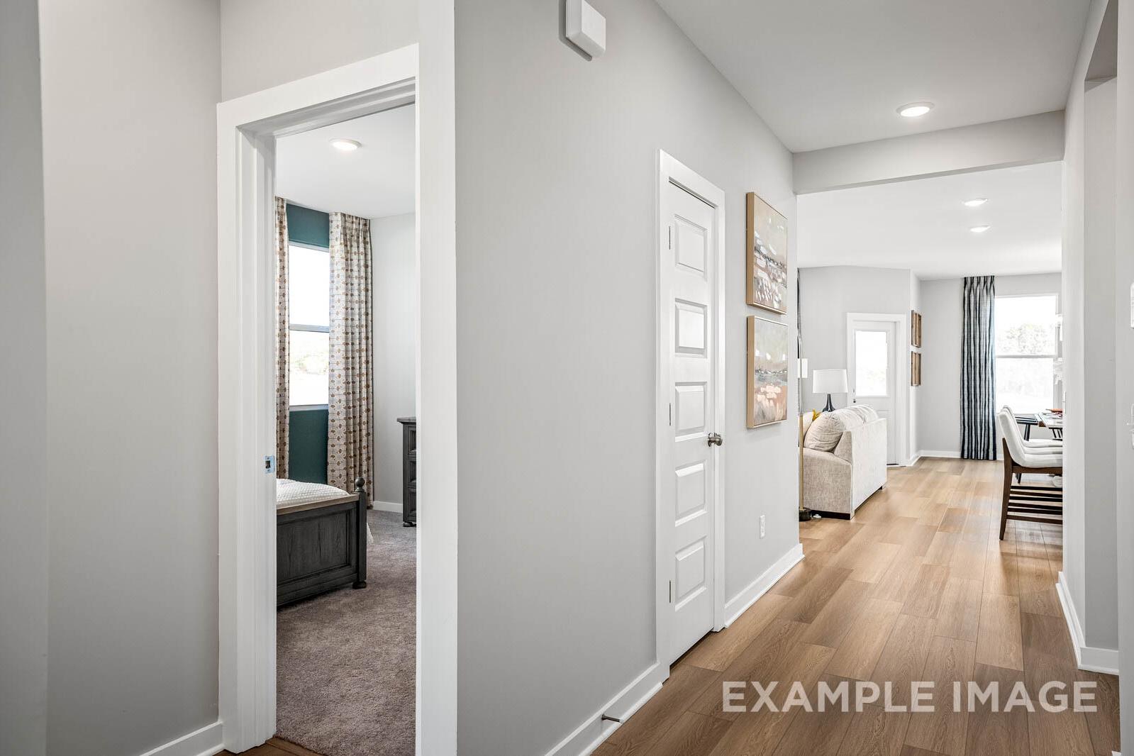 Spacious gray hallway in The Franklin B home leading to bedroom with bed and open living dining area on hardwood floors