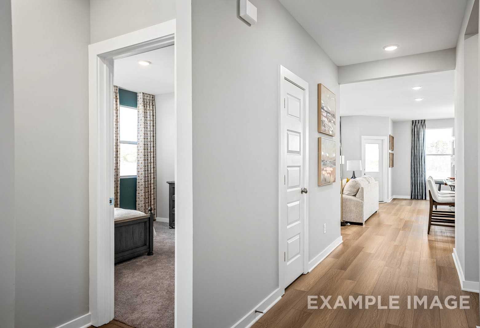 Hallway interior of The Franklin C home showcasing master bedroom with bed, open living and dining area, gray walls, hardwood floors