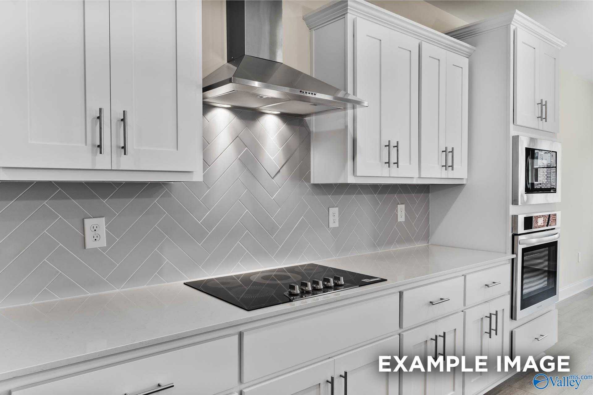 Modern kitchen featuring white cabinets, stainless steel hood, gray herringbone backsplash in Davidson Homes The Finleigh, Meridianville AL