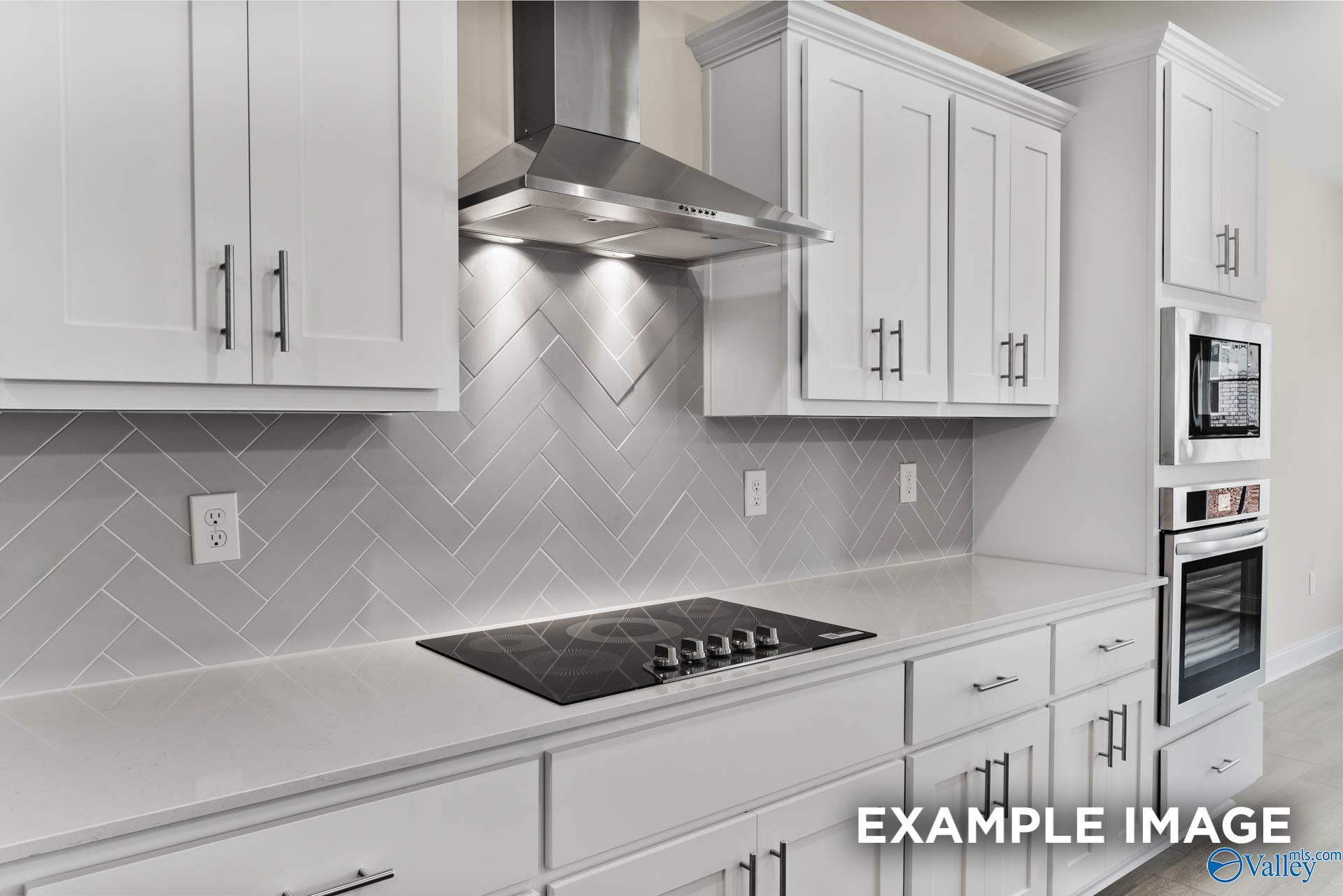 Modern white kitchen with herringbone gray backsplash, stainless hood, induction cooktop in Davidson Homes The Finleigh, Huntsville