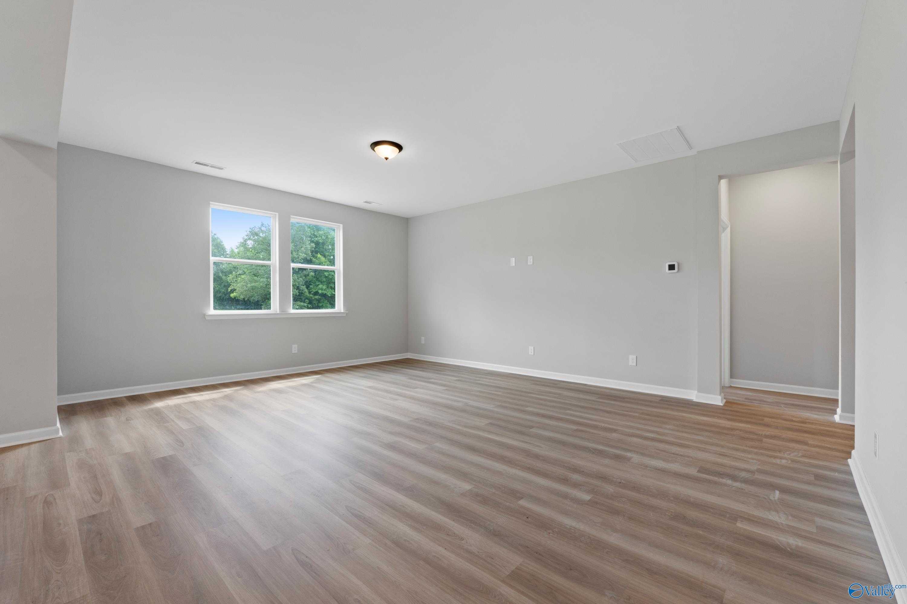 Bright empty bedroom with gray walls, large windows overlooking greenery, and warm luxury vinyl plank flooring in Davidson Homes The Dorado, Huntsville, Alabama