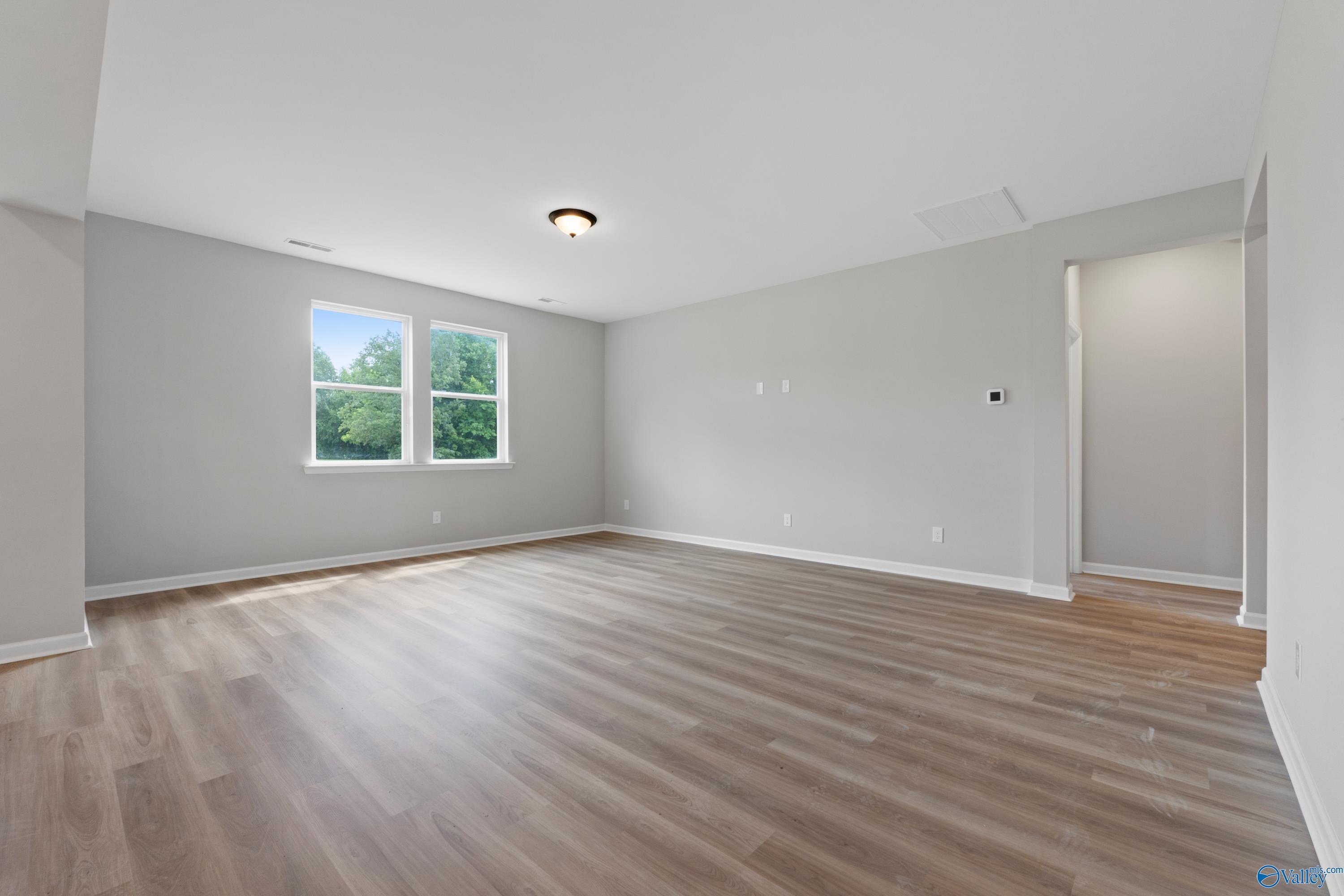 Bright empty bedroom with gray walls, large windows overlooking greenery, and warm luxury vinyl plank flooring in Davidson Homes The Dorado, Huntsville, Alabama