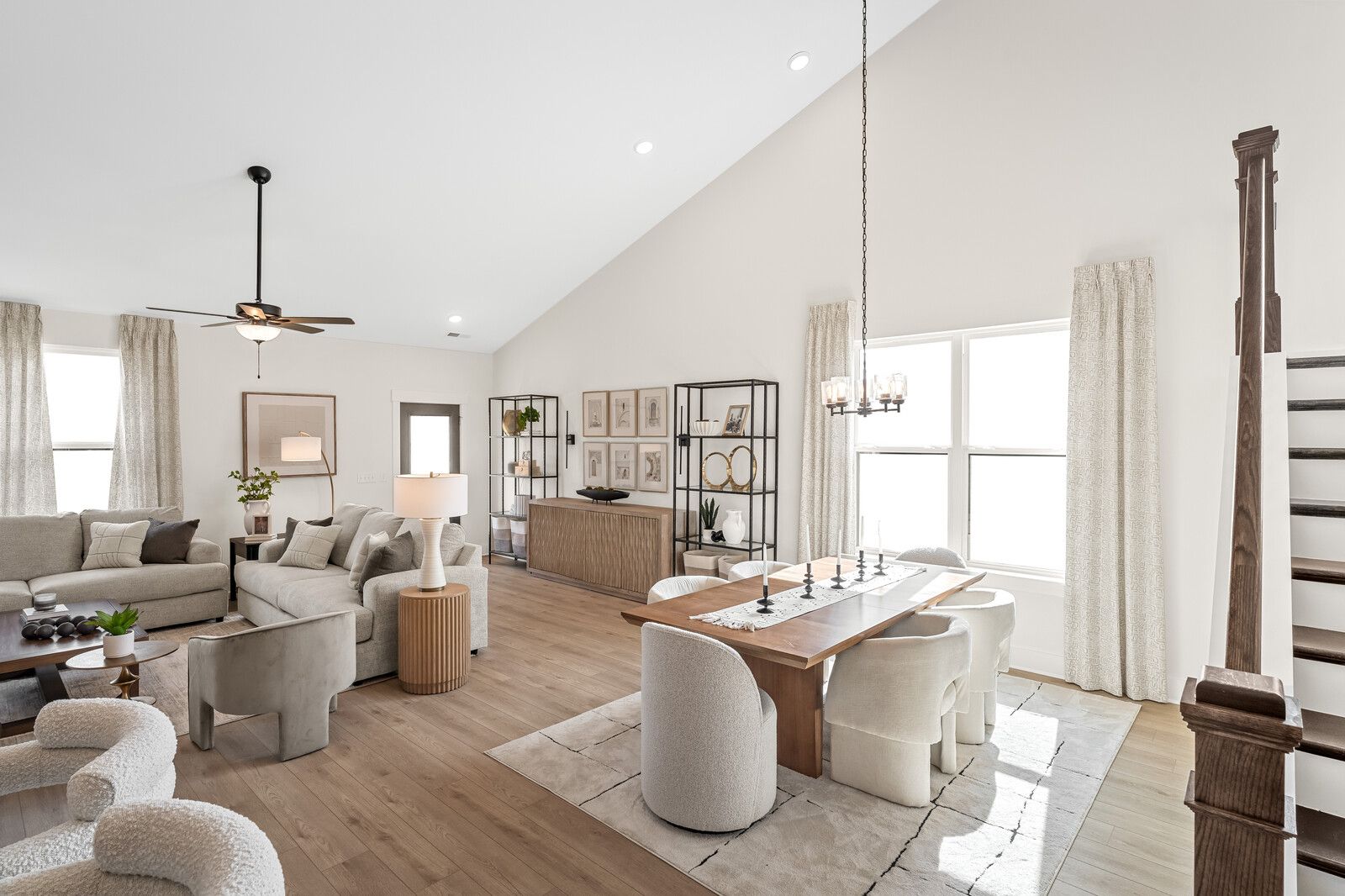 Open-concept living and dining area at Benders Cove in Mt. Juliet TN with hardwood floors, white staircase, plush seating, and large windows