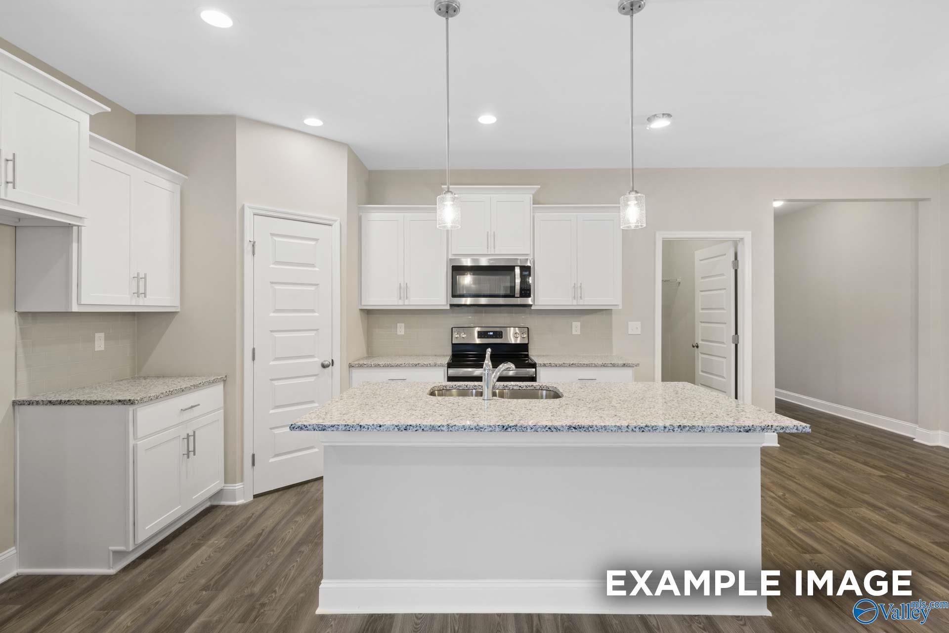 Open-concept kitchen with white cabinets, granite island, stainless appliances in Davidson Homes The Camilla A, Hartselle, Alabama