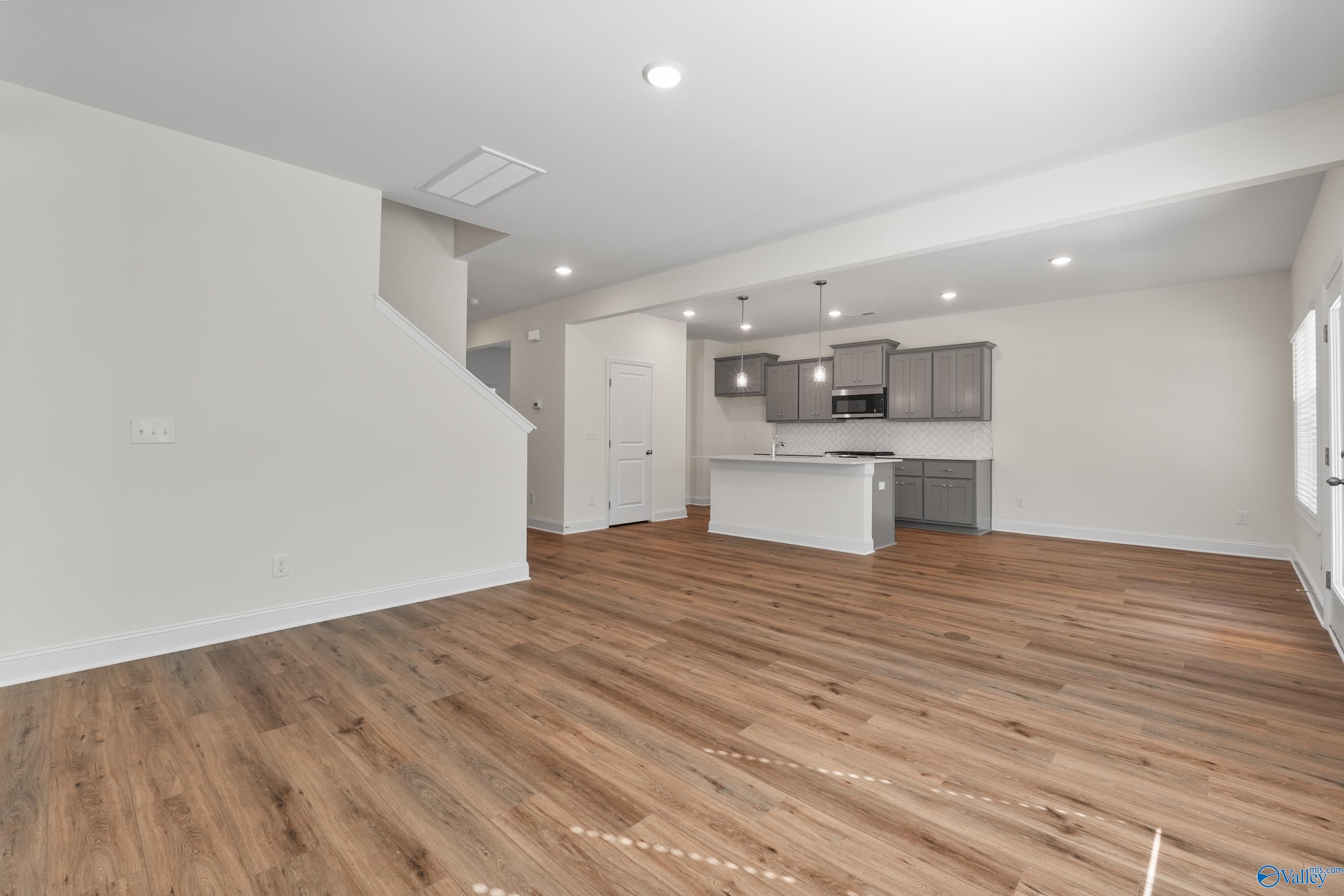 Open-concept kitchen with white island, gray shaker cabinets, hardwood floors, and adjacent stairs in Davidson Homes The Shelby A, Athens, Alabama