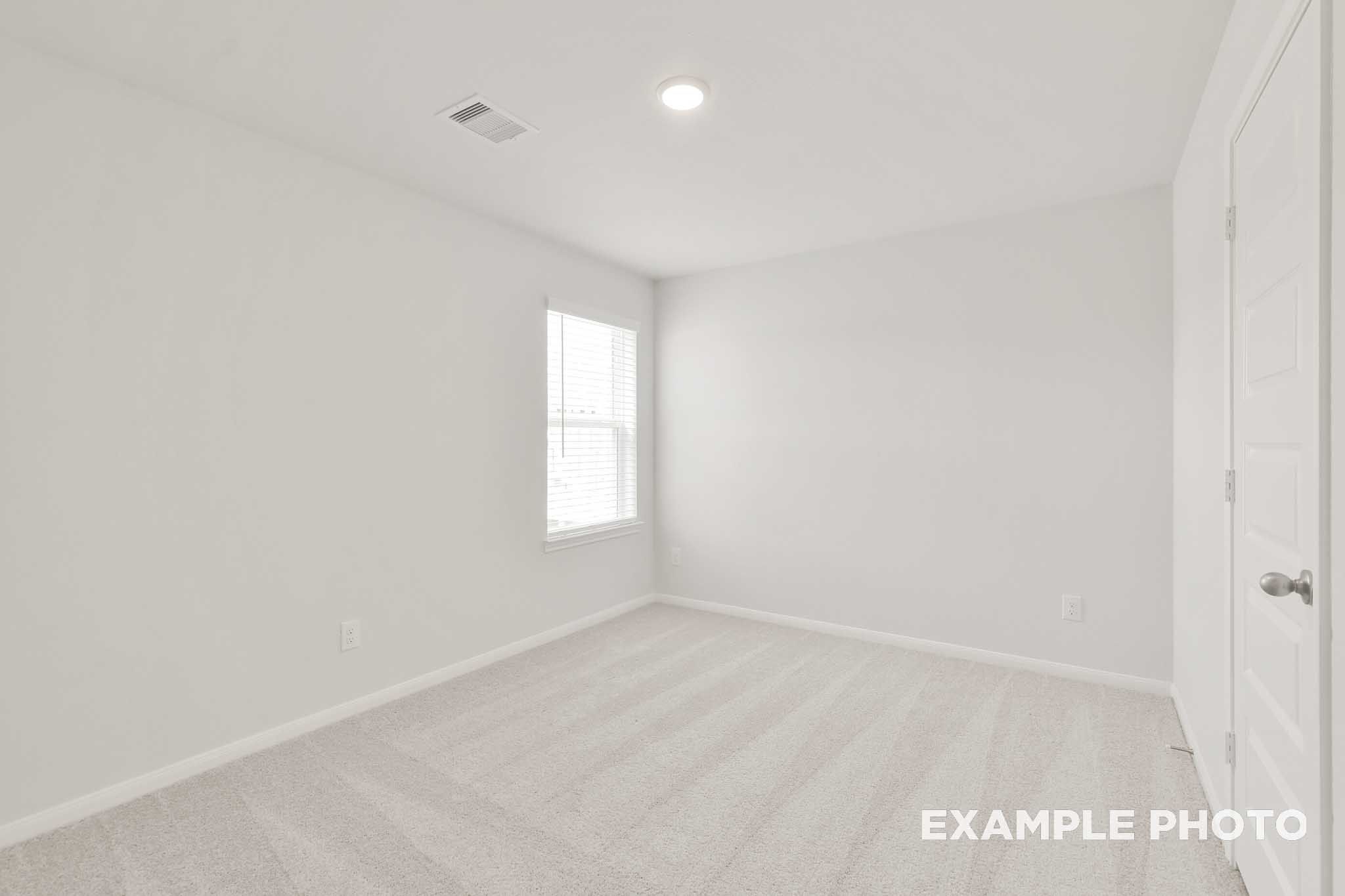 Bright empty bedroom in The Brazos by Davidson Homes, Beasley TX, featuring carpet flooring, white walls, and window with blinds.