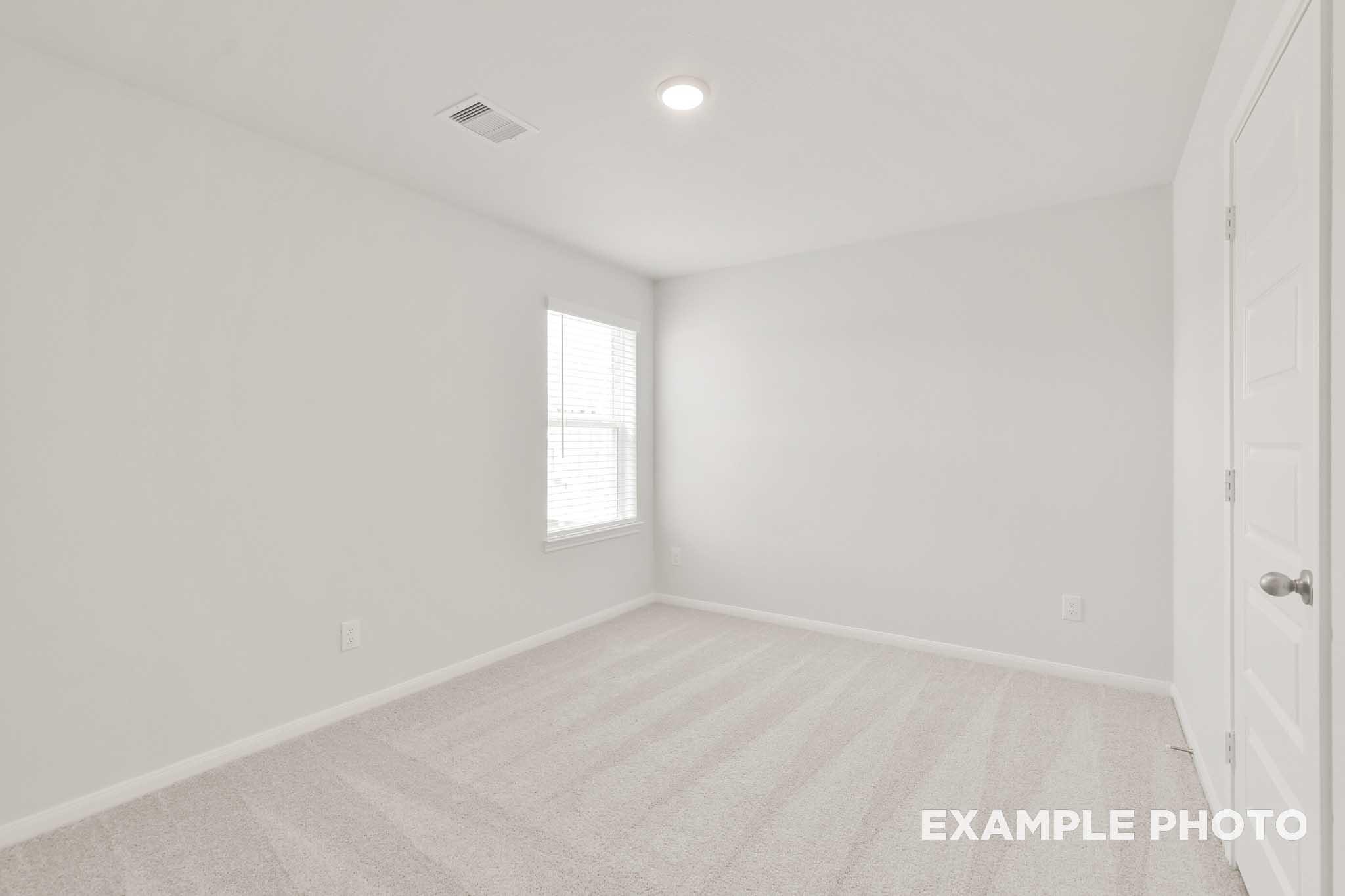 Bright empty bedroom in The Brazos by Davidson Homes, Beasley TX, featuring carpet flooring, white walls, and window with blinds.