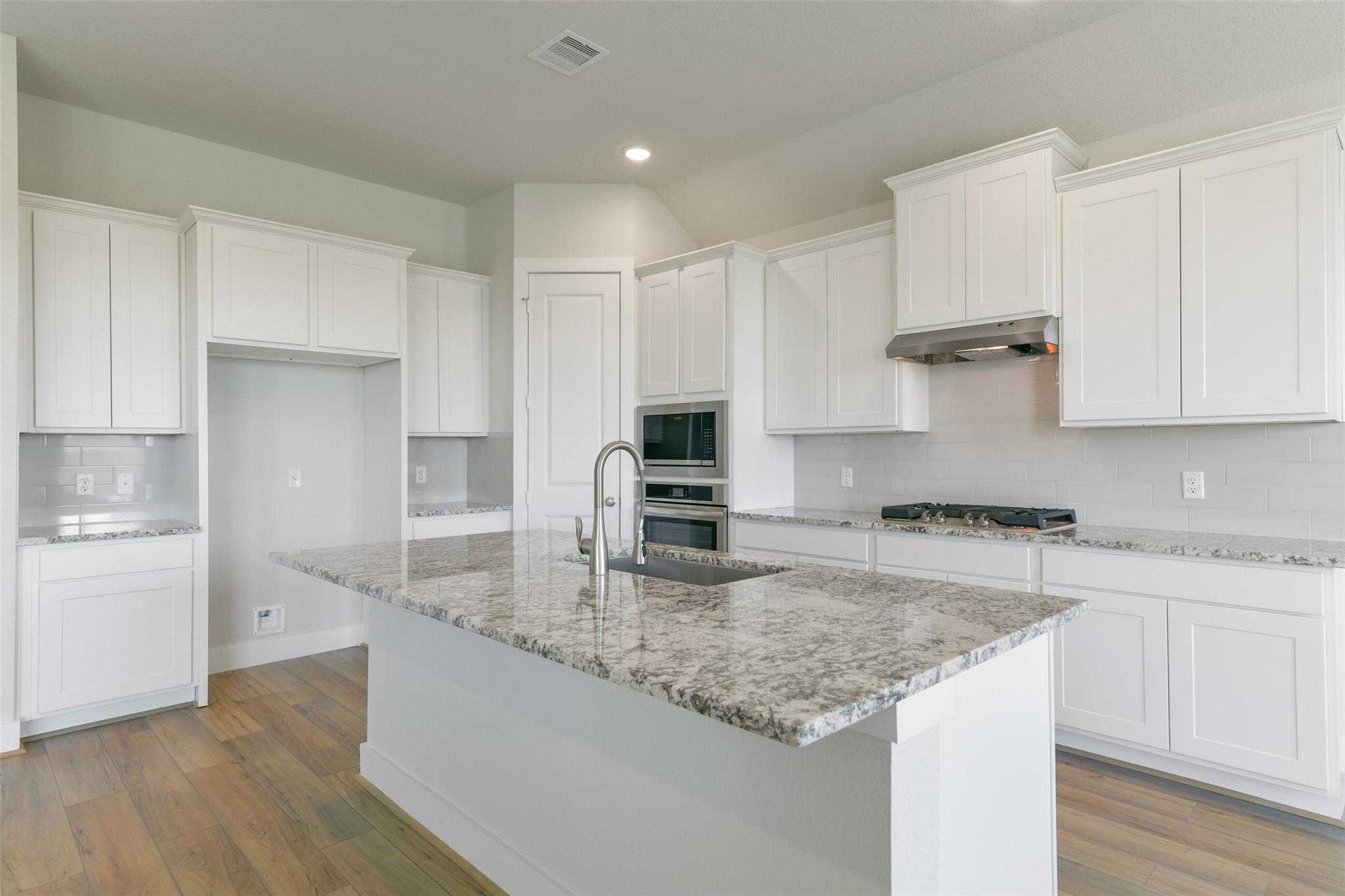 Modern white kitchen with granite island, stainless steel appliances, and open layout in Davidson Homes Edward A, Lago Mar, Texas City