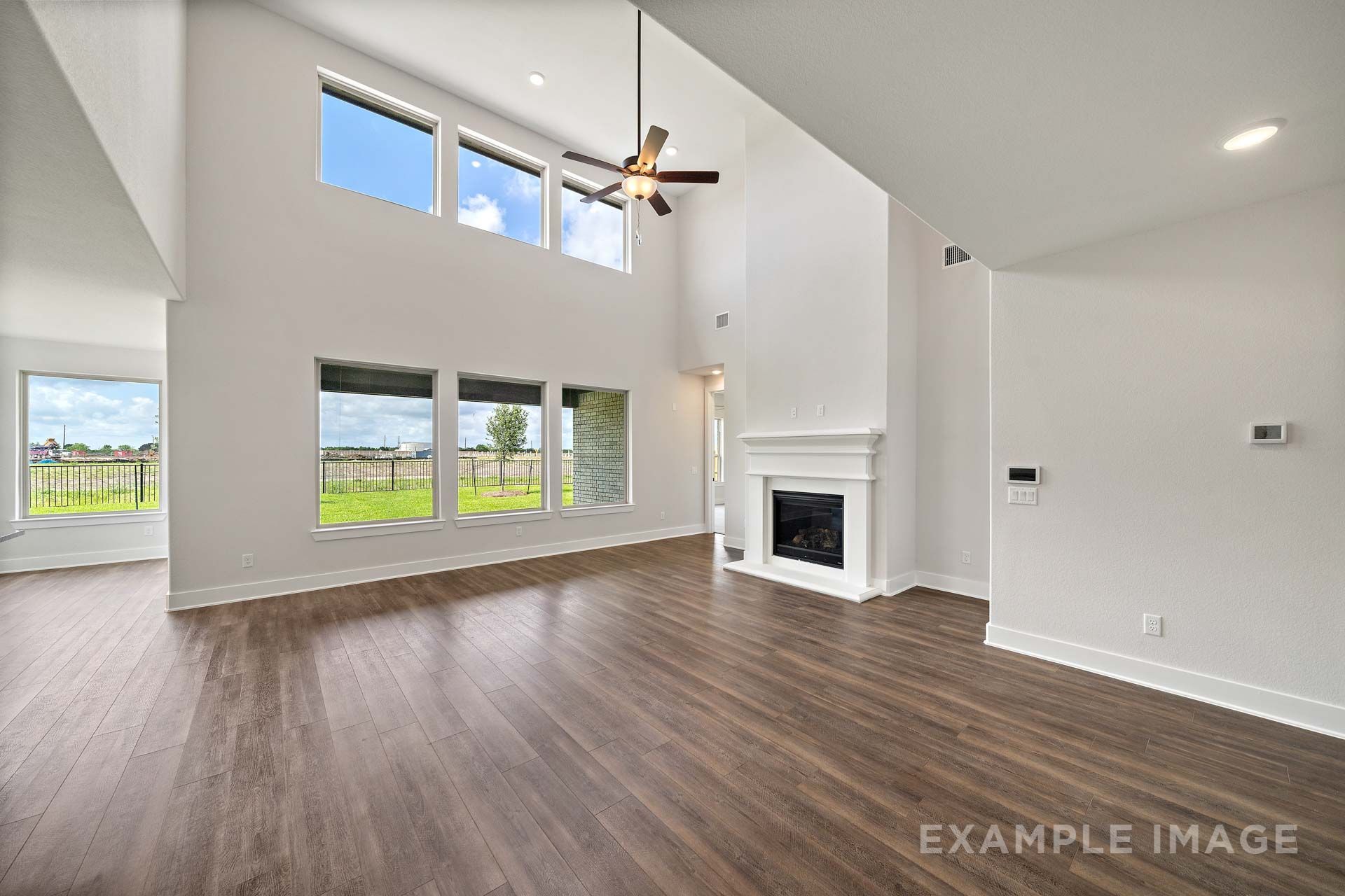Two-story great room in The Victoria by Davidson Homes with fireplace, wood-look flooring, and tall windows