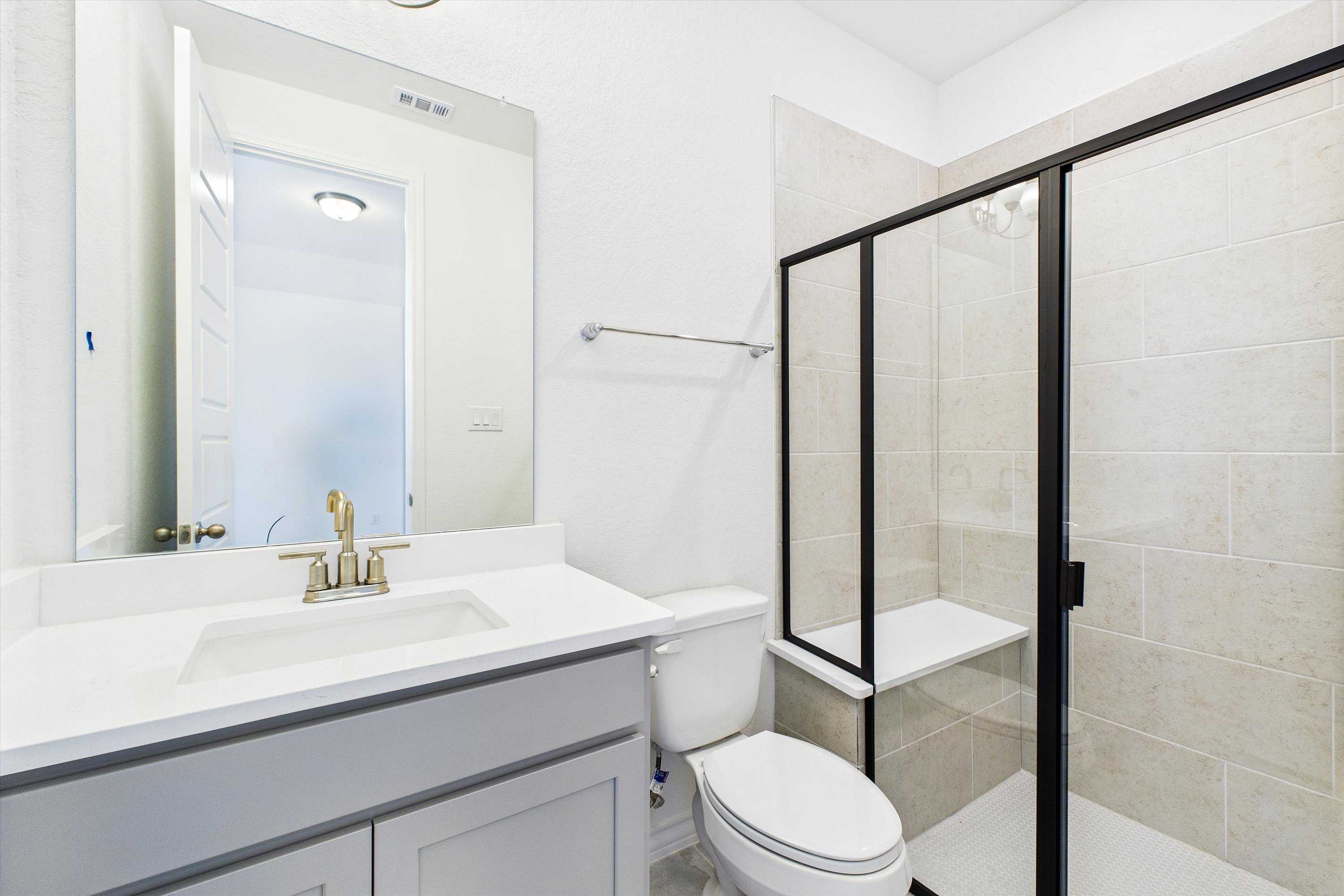Modern bathroom featuring gray vanity, frameless glass shower with beige tile in Davidson Homes The Summerlin C, Castroville, Texas