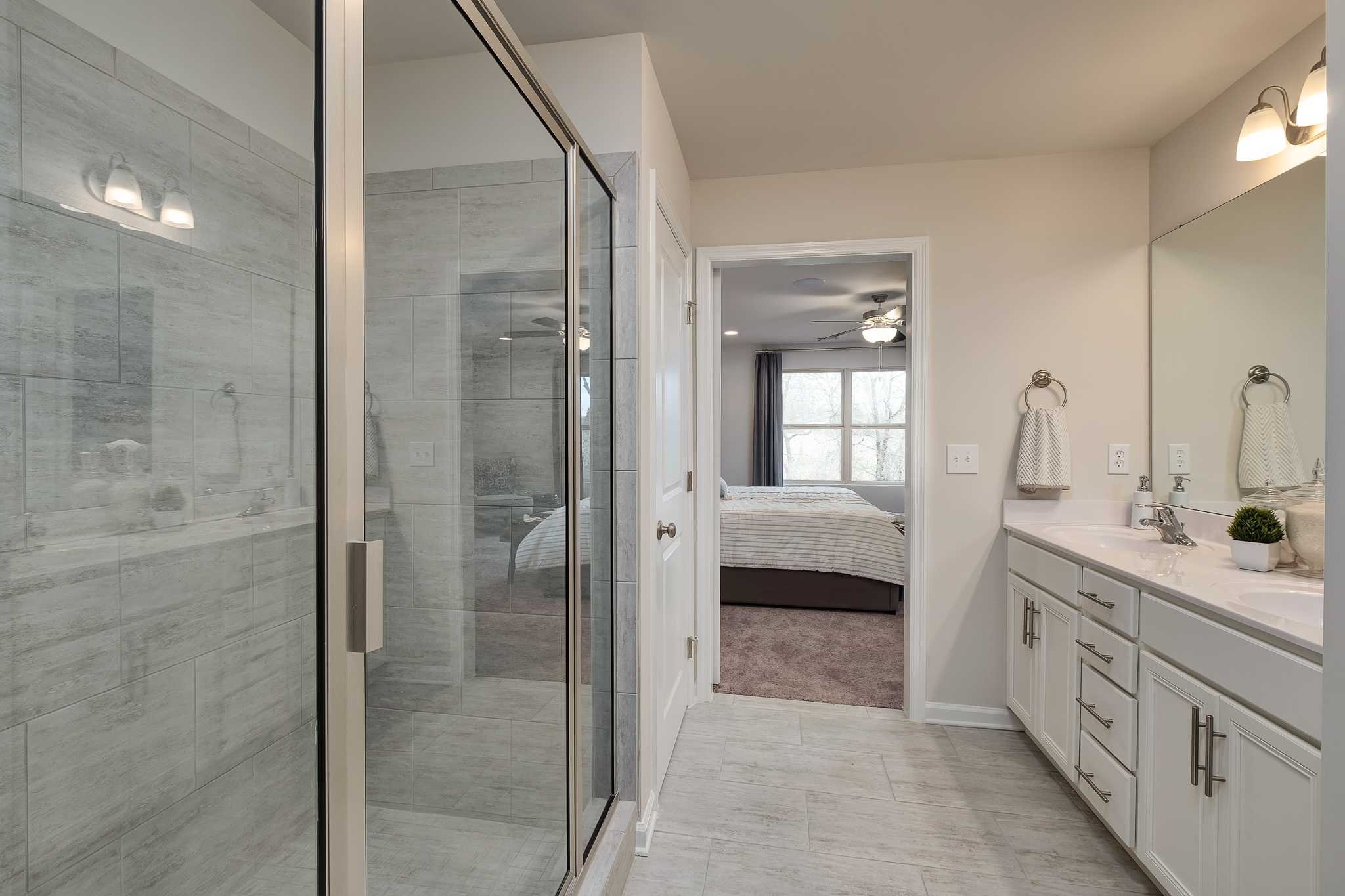 Spacious master bathroom at The Reserve at Overton in Hampton Cove AL with glass shower, double vanity, and bedroom view