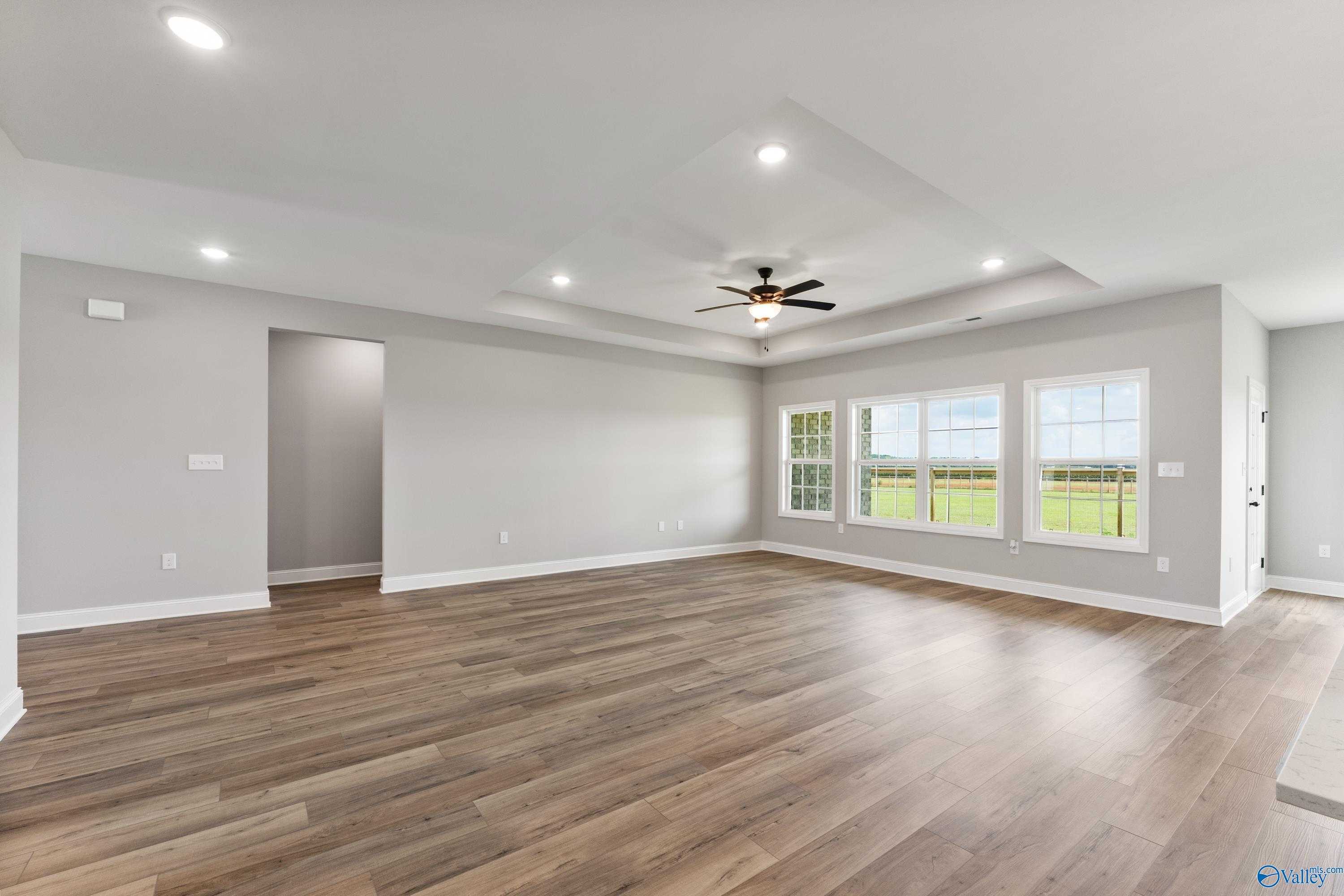 Spacious great room with hardwood floors, ceiling fan, recessed lights, and large windows overlooking fields in The Finleigh, Toney, Alabama