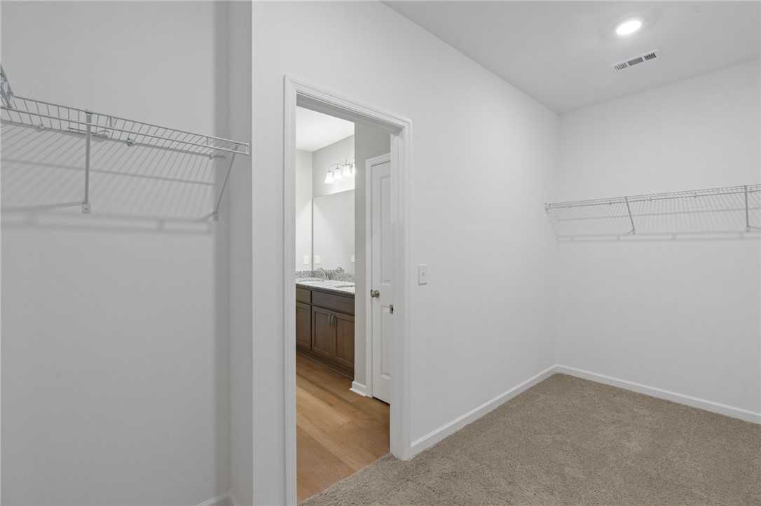 Spacious walk-in closet with wire shelving adjacent to modern master bathroom in Davidson Homes The Luna B, Opelika, Alabama