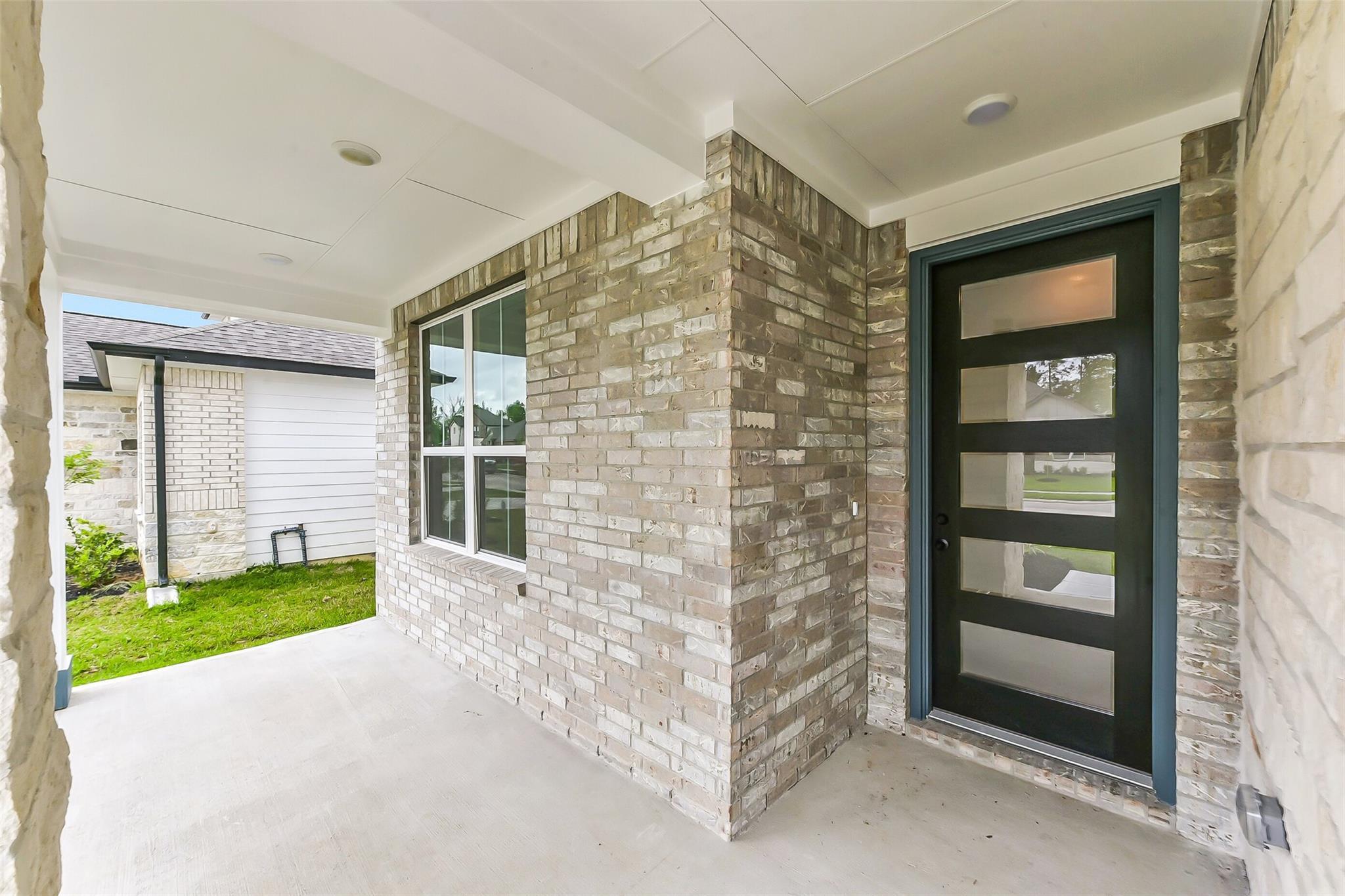Modern covered front porch with beige brick exterior and black frosted glass entry door in Davidson Homes The Sequoia C, Sundance Cove, Crosby Texas