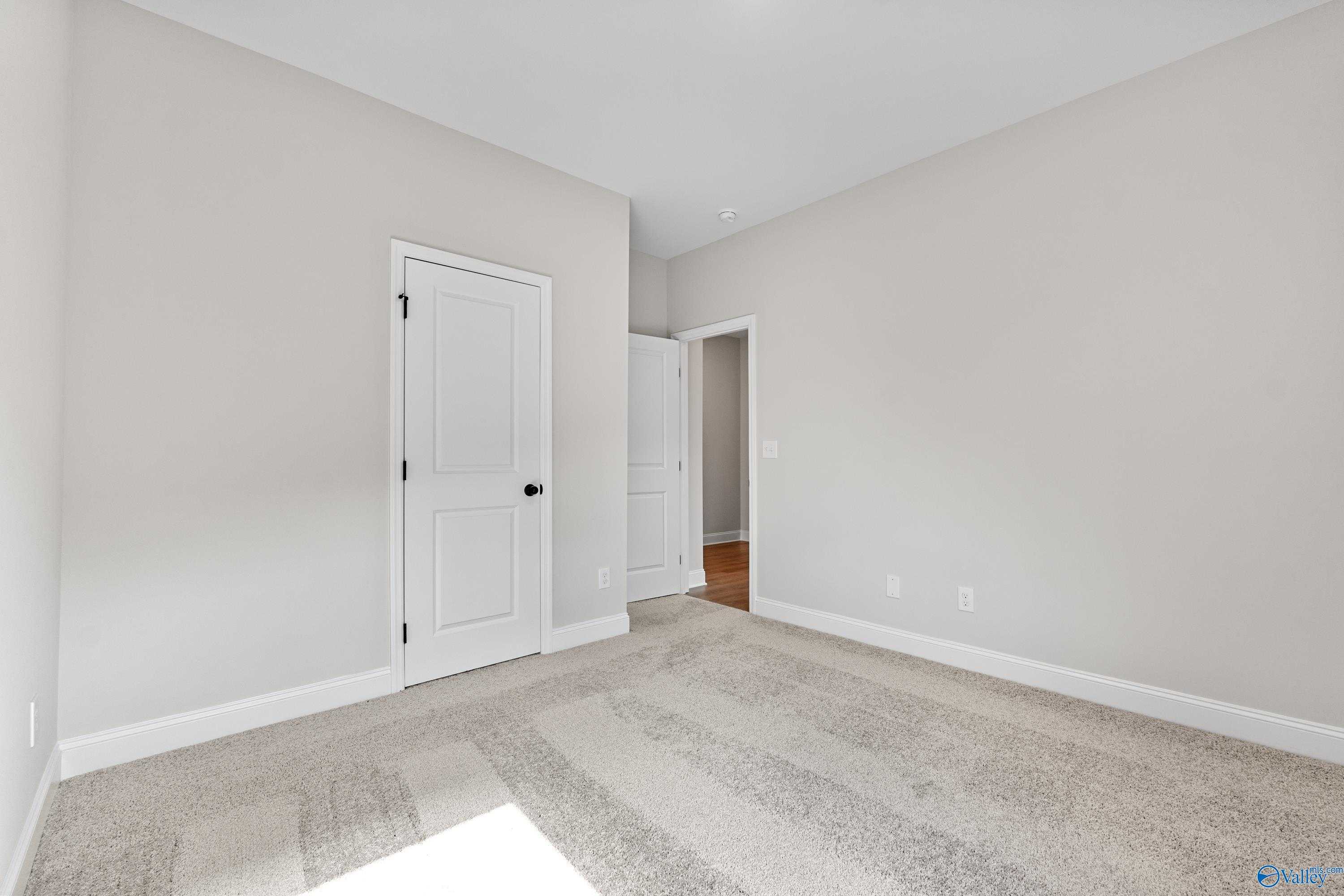 Empty secondary bedroom featuring light gray walls, white doors, and plush carpet in Davidson Homes The Franklin B, Hazel Green, Alabama