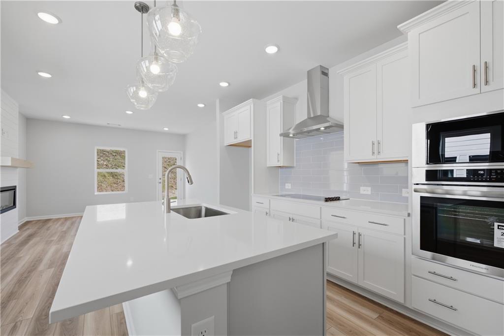 White kitchen with large island, pendant lights, stainless appliances, and luxury vinyl plank flooring in The Oconee B plan, Canton GA