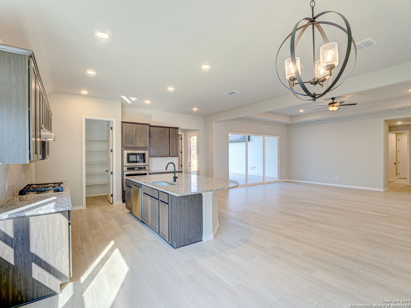 Modern open-concept kitchen with gray cabinets, quartz island, stainless appliances, chandelier, open to living area in The Summerlin A, Castroville TX