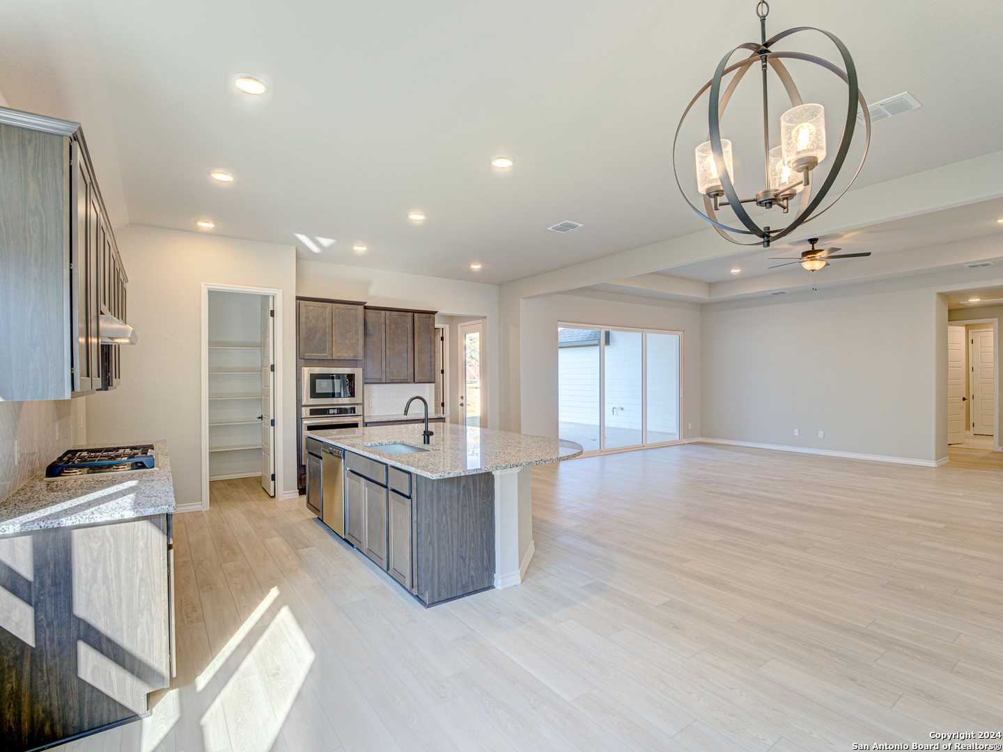 Modern open-concept kitchen with gray cabinets, quartz island, stainless appliances, chandelier, open to living area in The Summerlin A, Castroville TX
