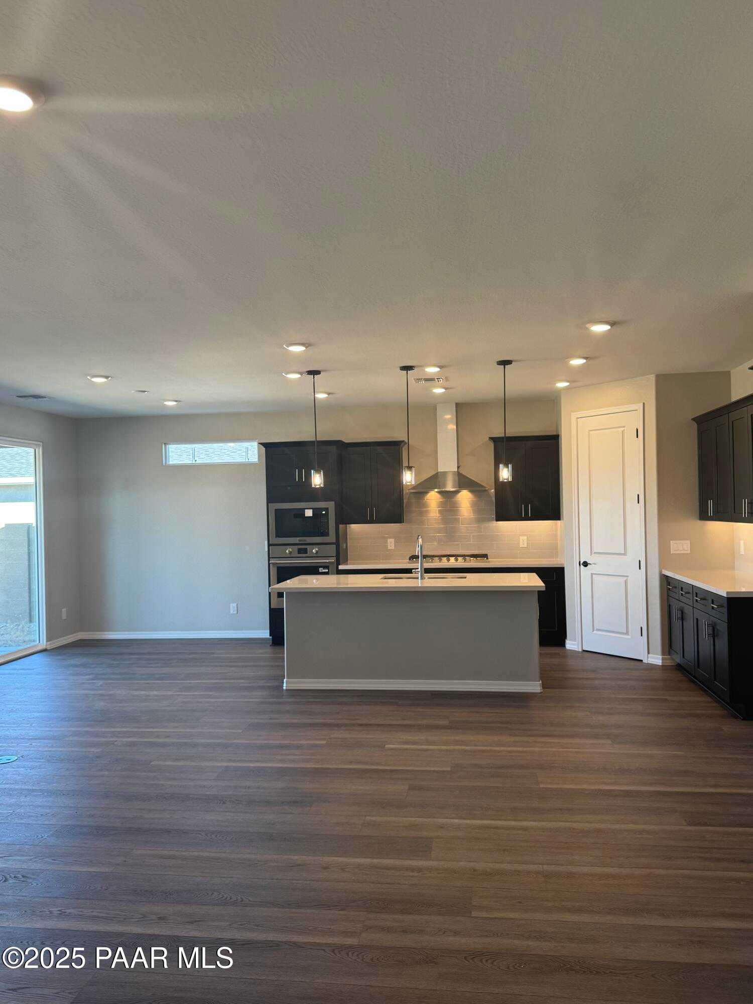Modern open-concept kitchen featuring large gray island, black cabinets, stainless appliances, and hardwood floors in Davidson Homes Durango II A, Prescott AZ