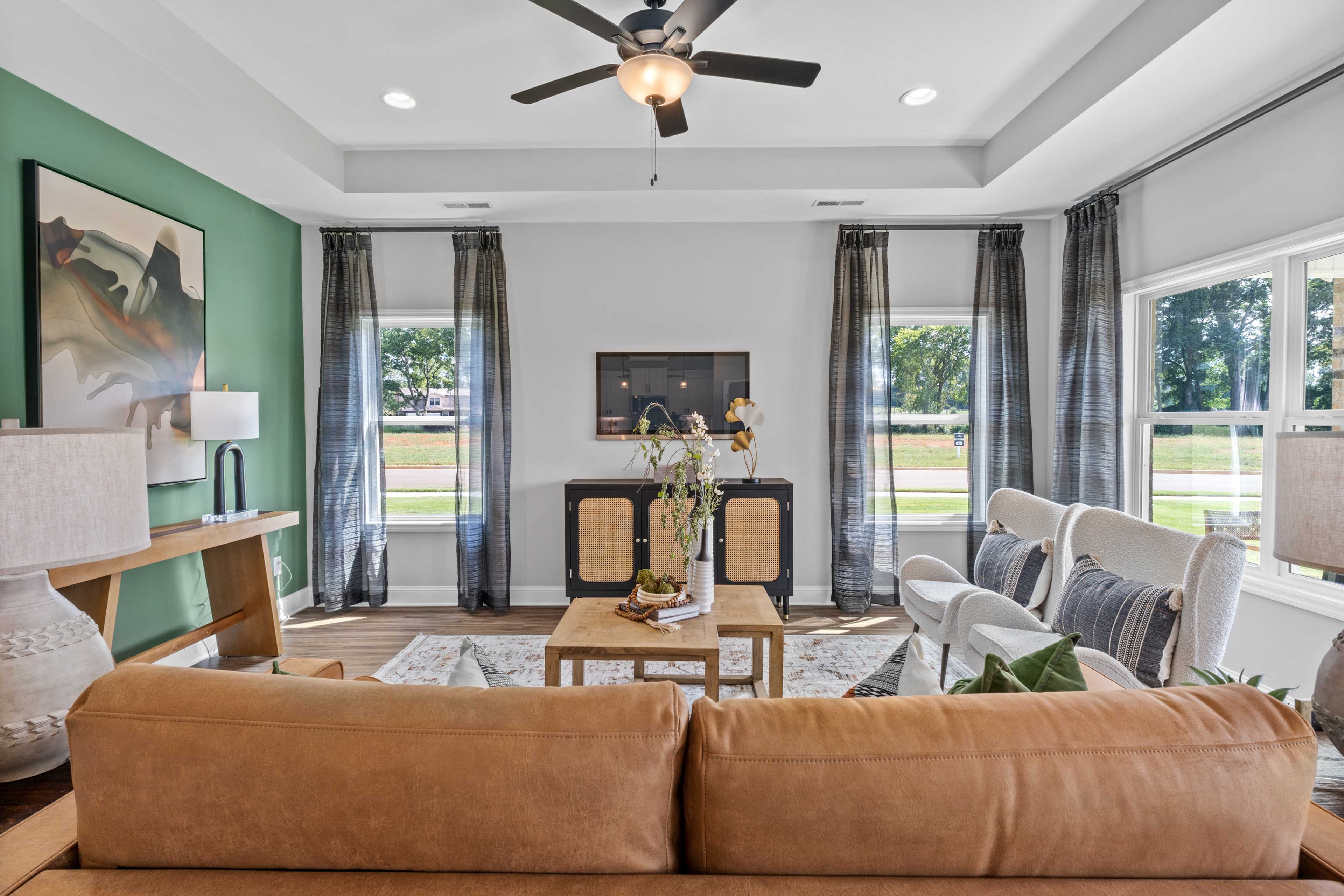 Modern living room at Wood Trail in Toney AL with leather sectional sofa, wooden coffee table, large windows, ceiling fan, and abstract art