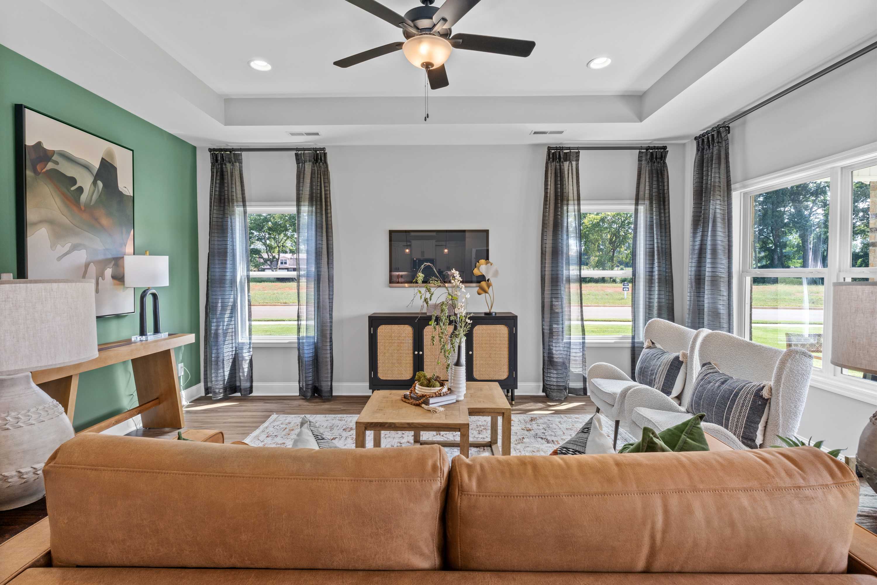Modern living room at Wood Trail in Toney AL with leather sectional sofa, wooden coffee table, large windows, ceiling fan, and abstract art