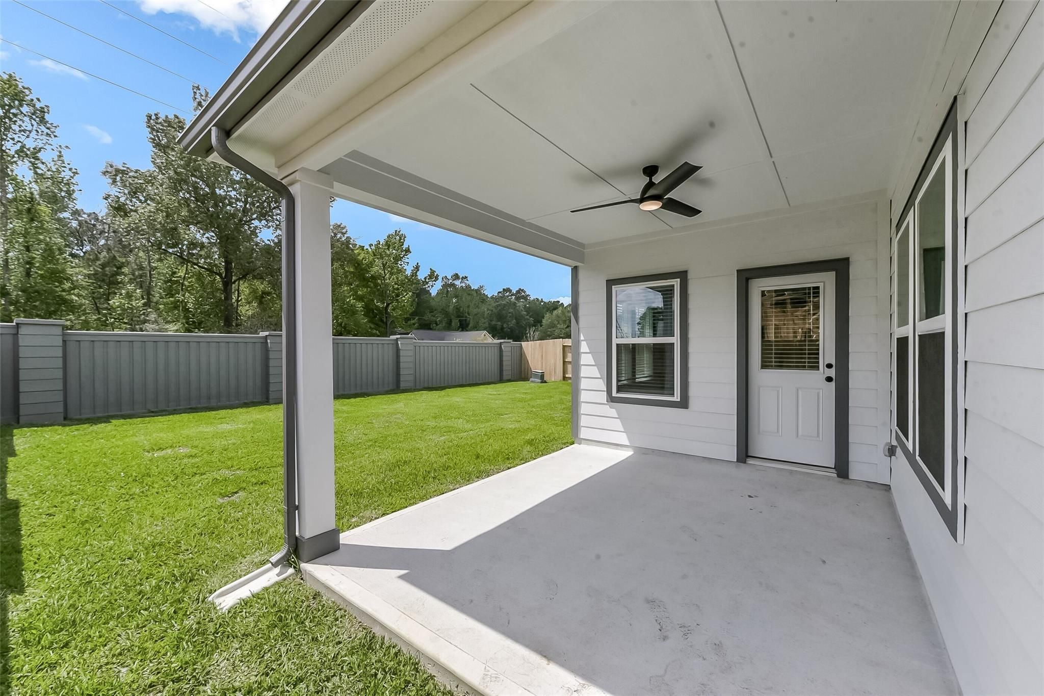 Covered back patio with ceiling fan, white house exterior, lush green lawn, and fenced yard in Davidson Homes The Everett C, Sundance Cove, Crosby, Texas