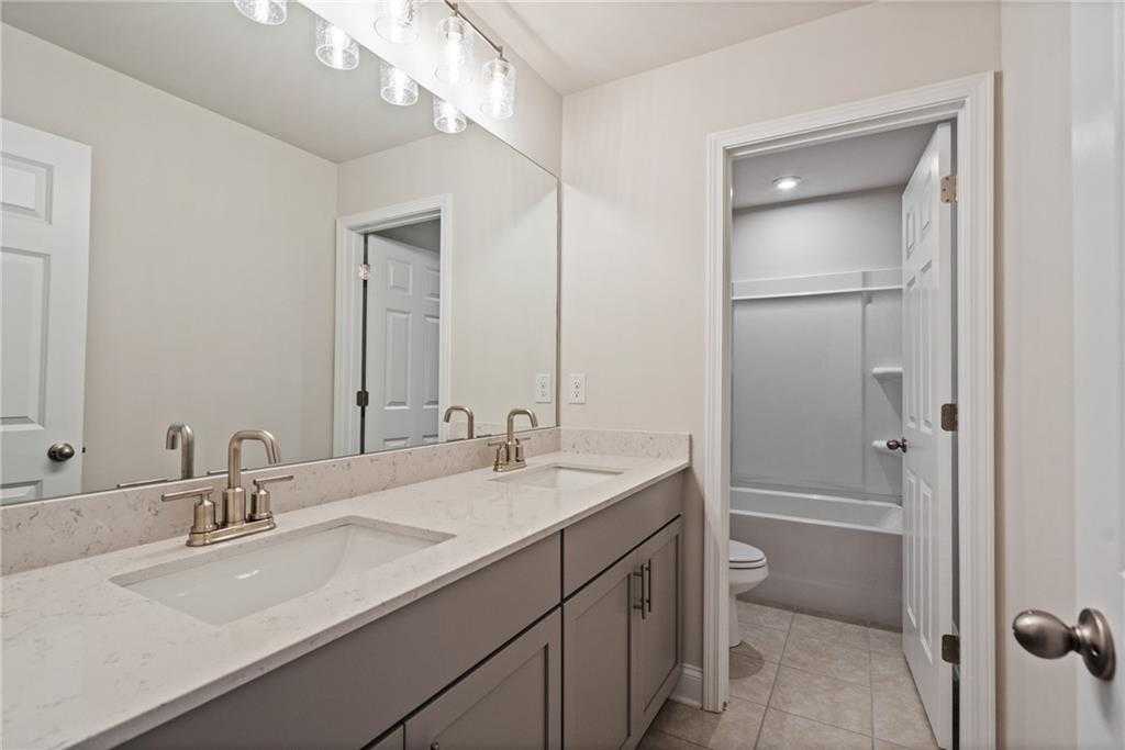 Modern double-sink vanity with quartz tops, gray cabinets, mirrors, and adjacent bathtub in Davidson Homes The Hickory B at Wehunt Meadows, Hoschton, GA