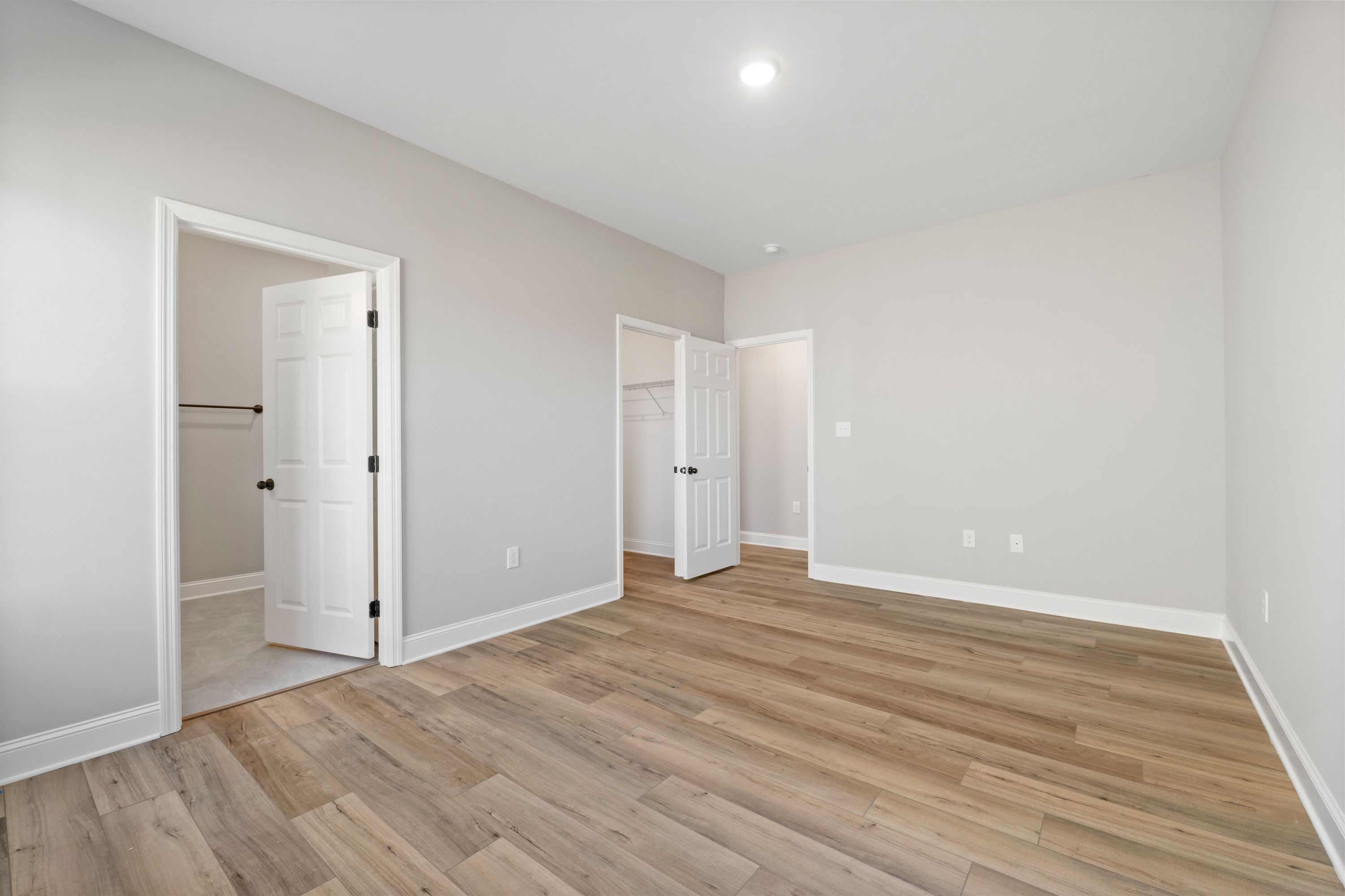 Spacious master bedroom in The Valencia with open walk-in closets, en-suite bath door, light gray walls, and light hardwood floors