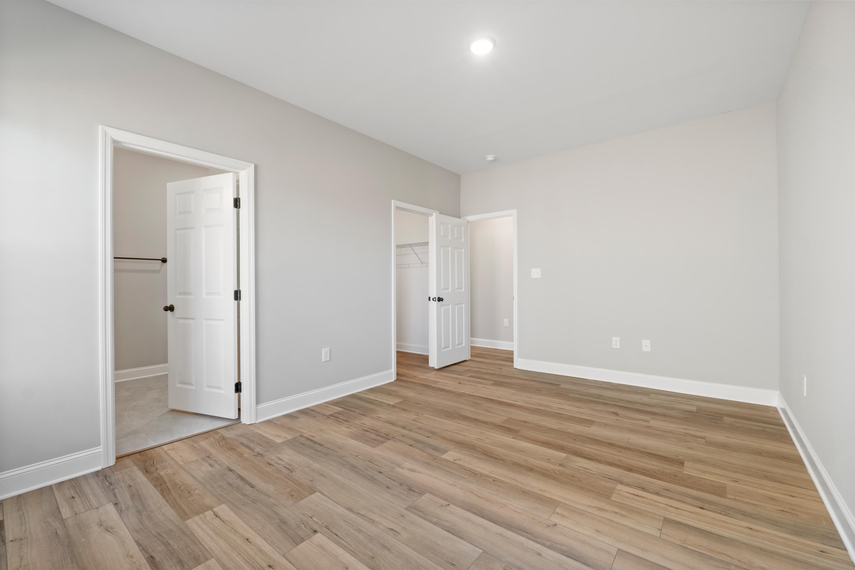 Spacious master bedroom in The Valencia with open walk-in closets, en-suite bath door, light gray walls, and light hardwood floors
