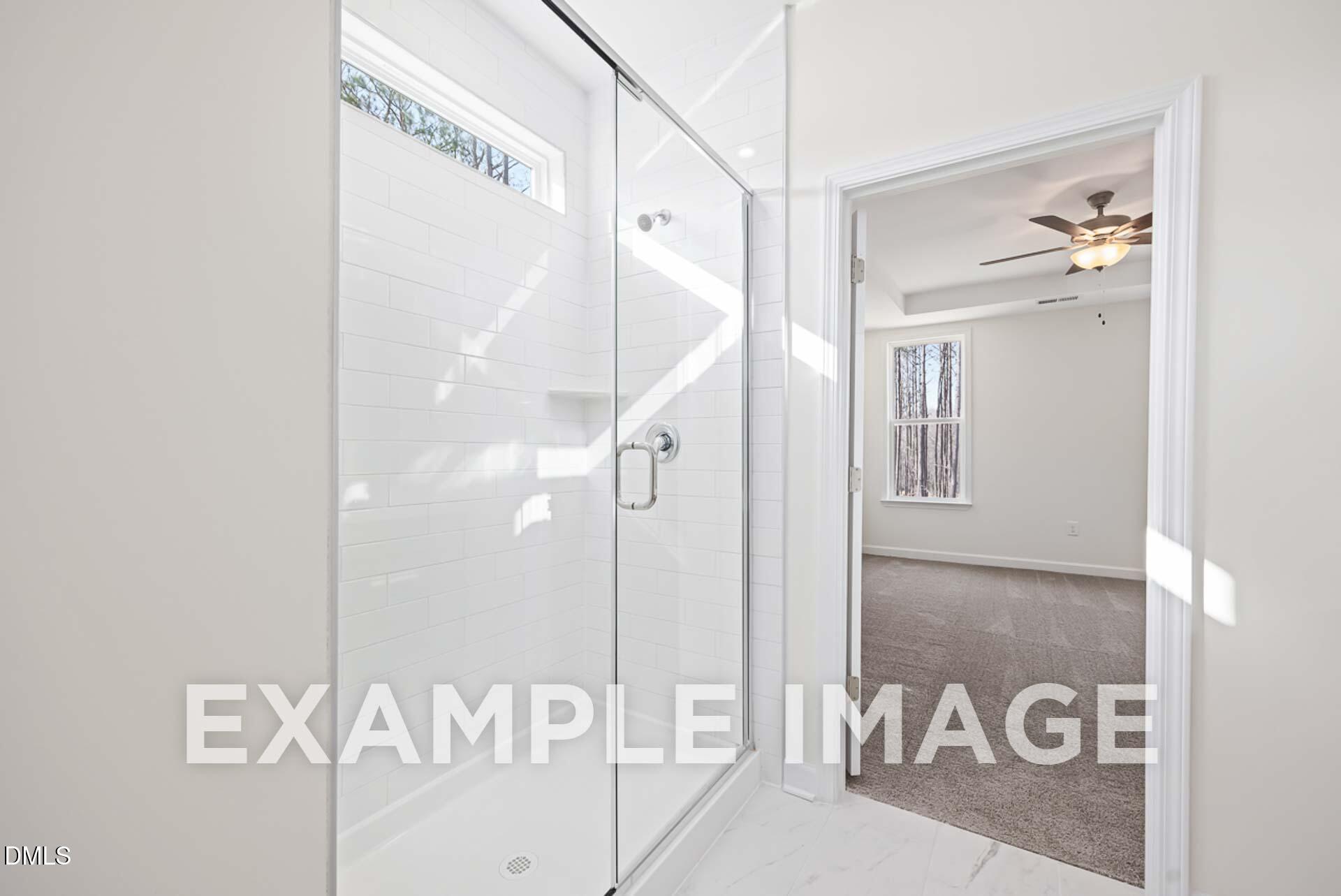 Modern white-tiled walk-in shower with frameless glass door adjacent to carpeted bedroom in The Ash B, Davidson Homes, Zebulon, NC