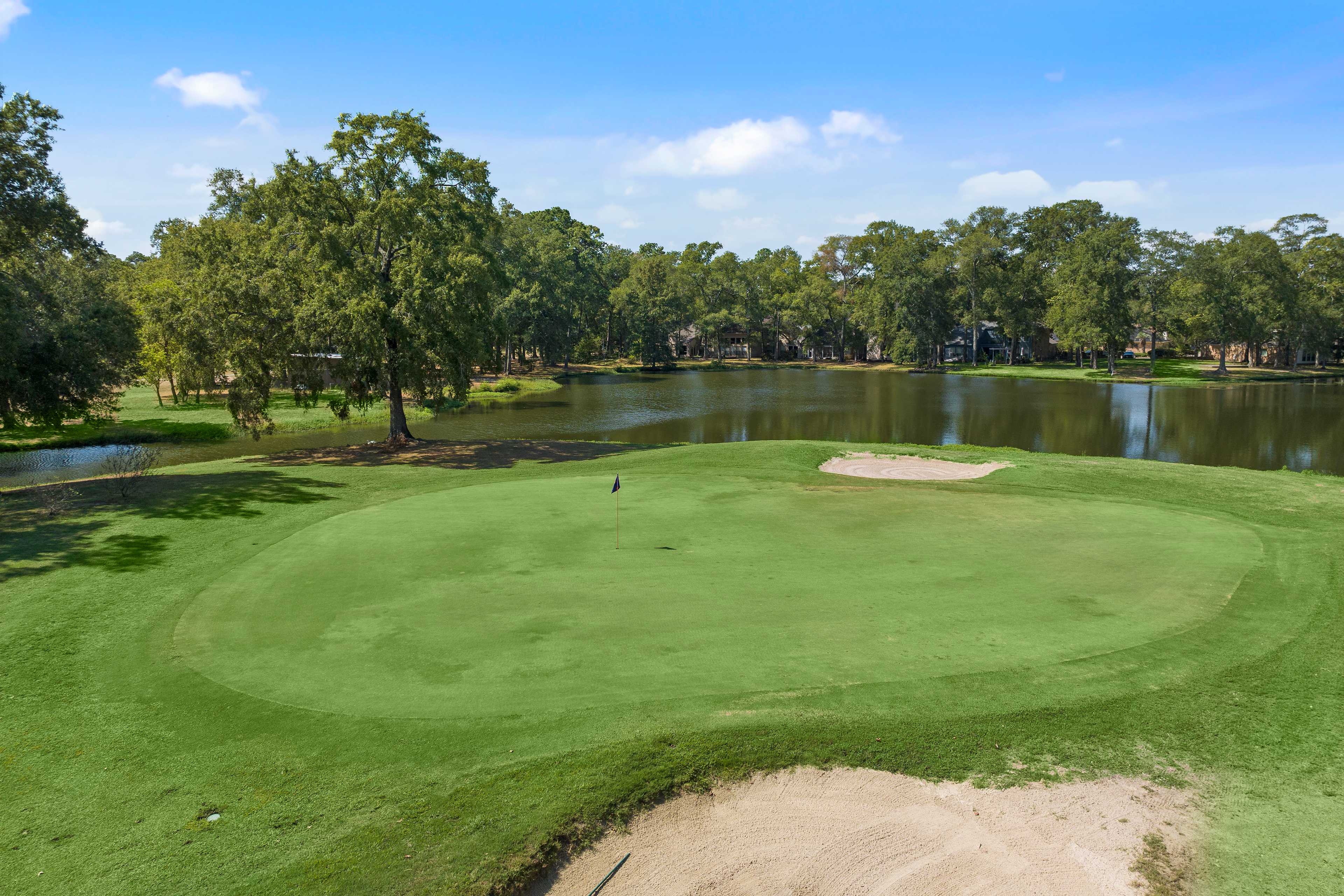 Lush golf green and sand bunker at Enclave at Newport in Crosby Texas with serene pond and oak trees