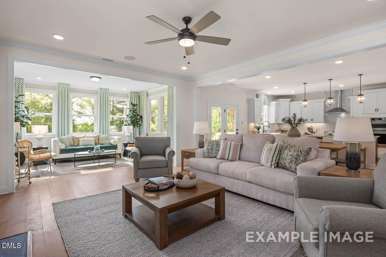 Bright open living room with plush neutral sofas, ceiling fan, and adjacent white kitchen in Davidson Homes The Crawford D, Angier, NC