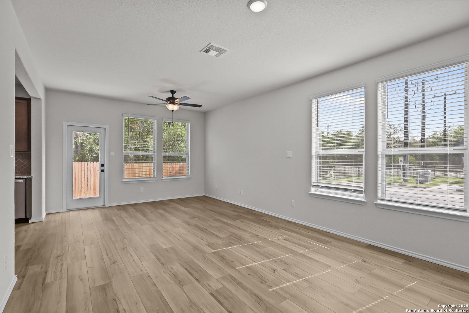 Spacious living room with hardwood floors, ceiling fan, large windows, and backyard access in Davidson Homes The Florence C, San Antonio TX
