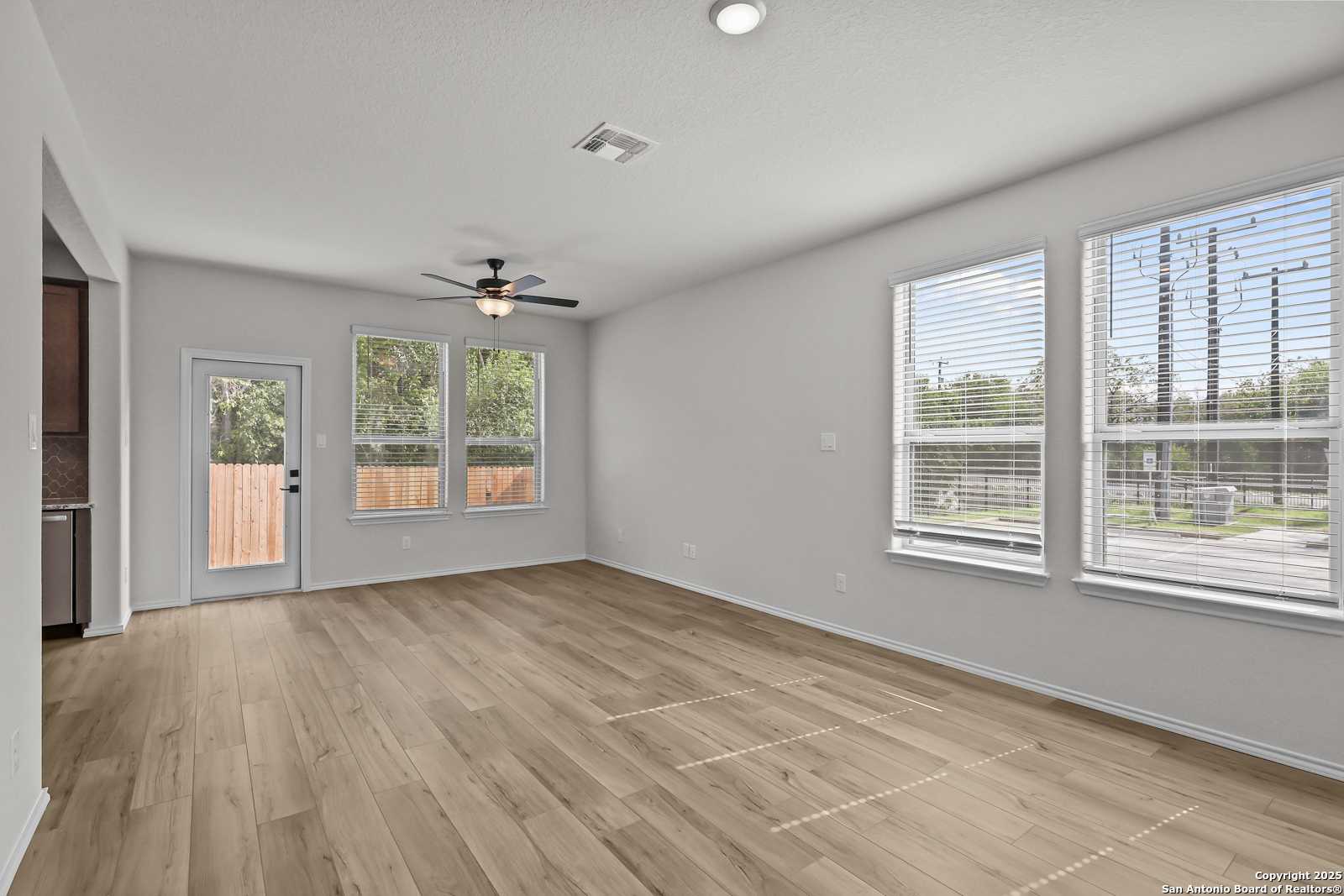 Spacious living room with hardwood floors, ceiling fan, large windows, and backyard access in Davidson Homes The Florence C, San Antonio TX