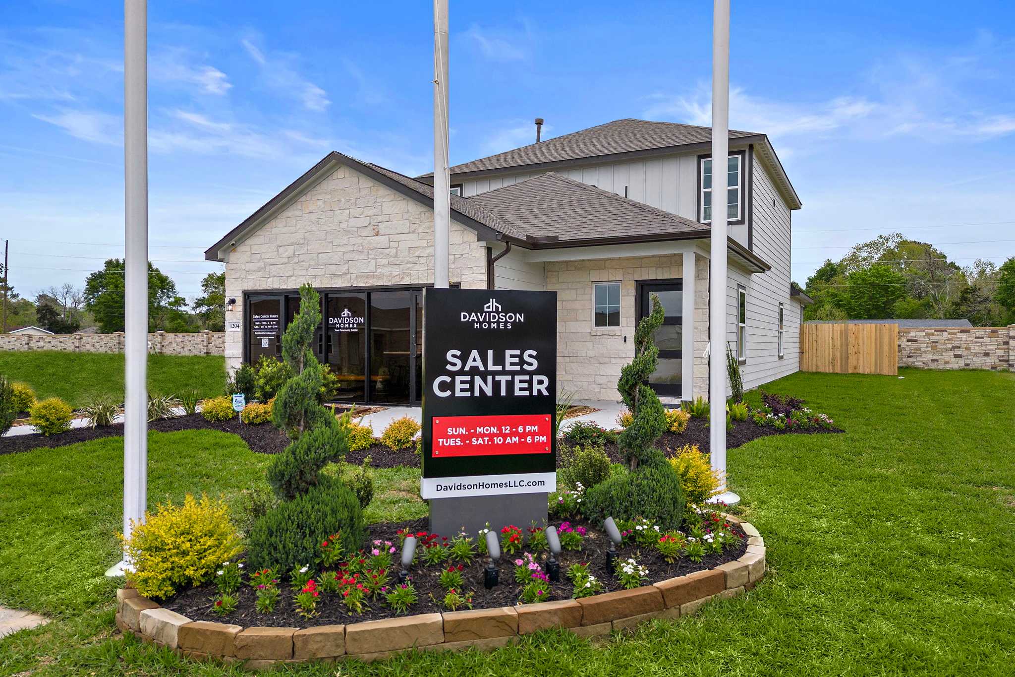 Davidson Homes sales center at The Villages at WestPointe in Dayton Texas with stone model home, flagpoles and landscaped flower beds