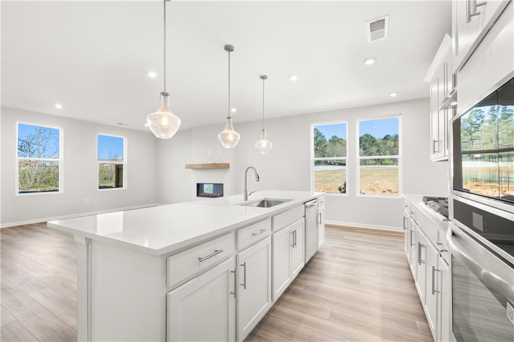 Modern white kitchen island with sink, stainless appliances, pendant lights, and wooded views in Davidson Homes The Cary A, Winder, GA