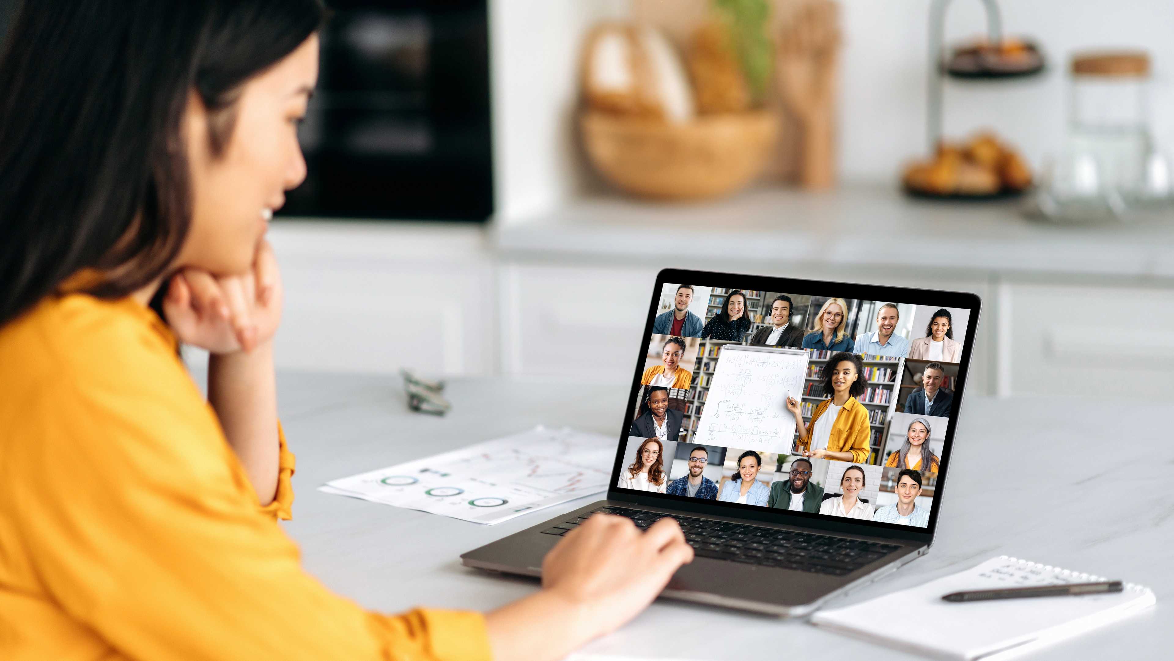 Woman attending virtual homebuyer seminar on laptop in cozy kitchen, viewing multiple participants