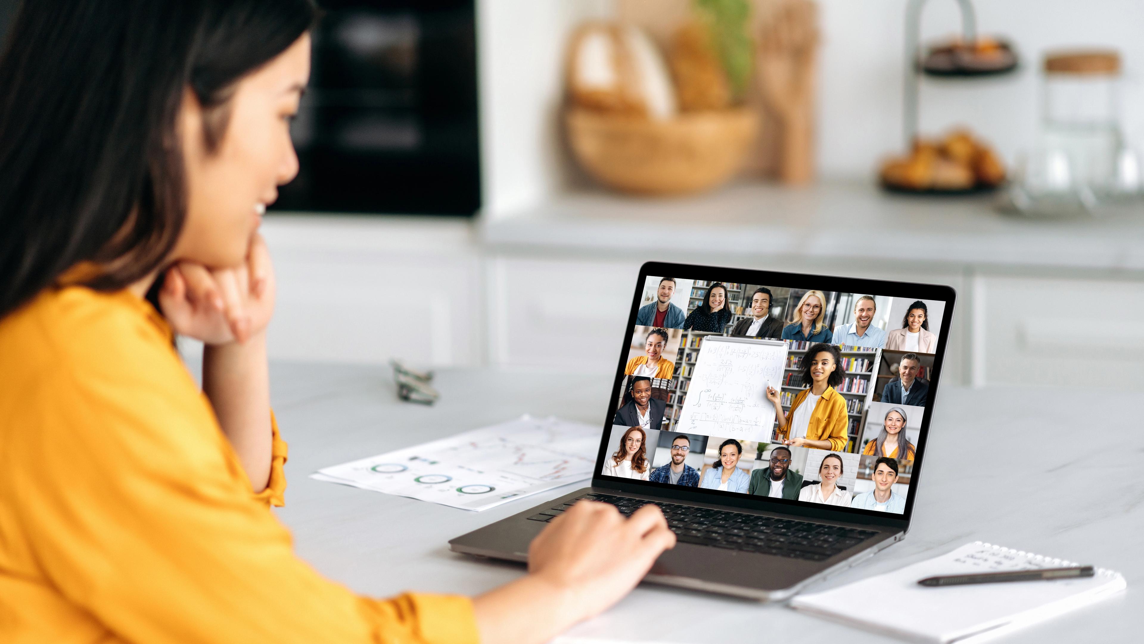 Woman attending virtual homebuyer seminar on laptop in cozy kitchen, viewing multiple participants