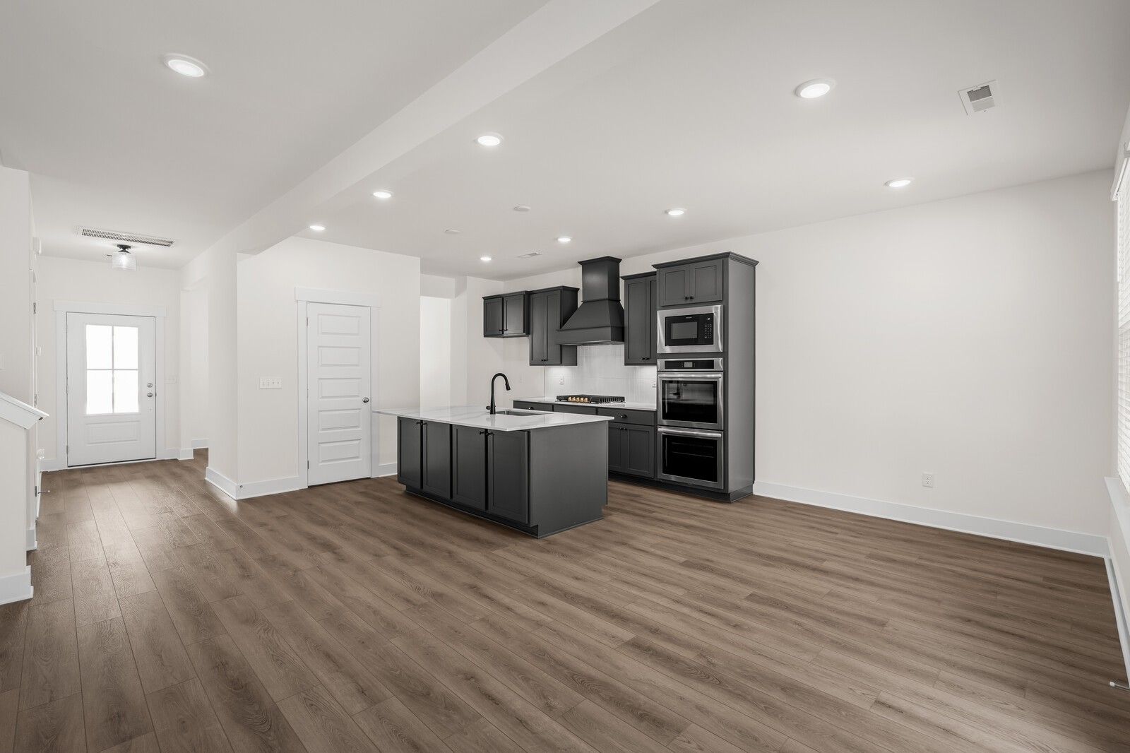 Modern kitchen with dark cabinetry, center island, and wood flooring in The Willow floor plan at Woods Crossing, Gallatin.