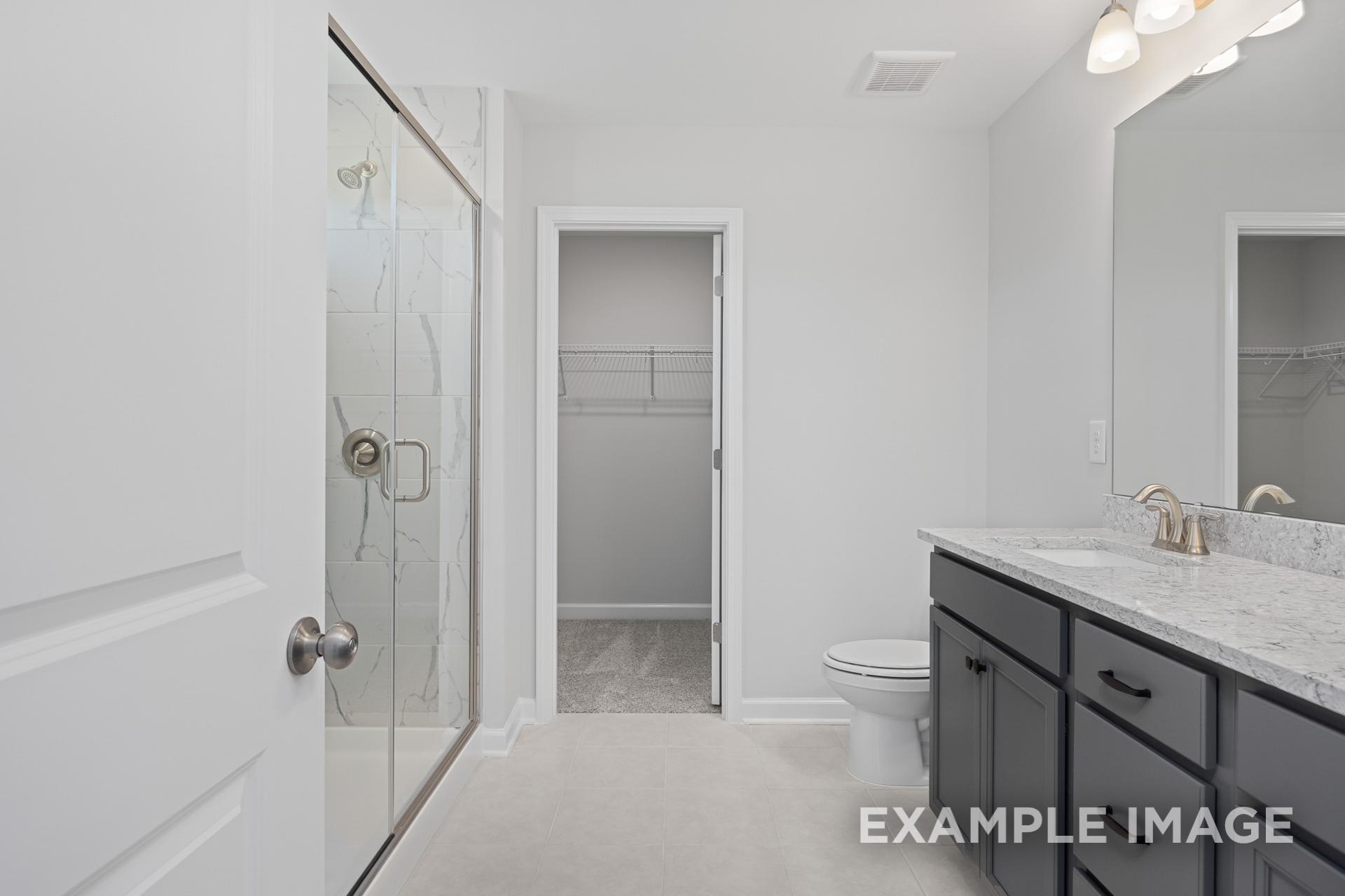 Spacious master bathroom in The Grace C with frameless glass shower, double vanity, quartz counters, and walk-in closet