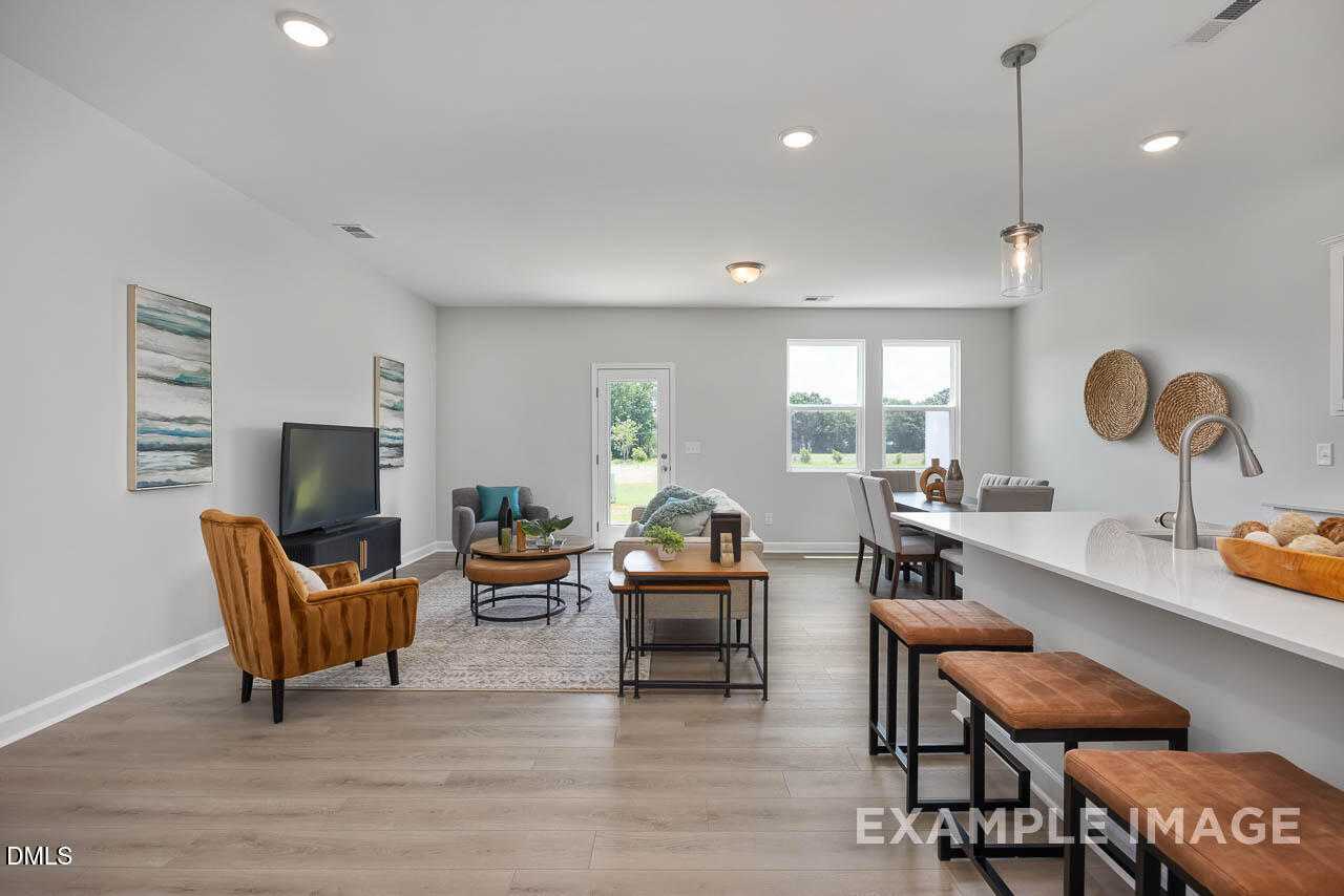 Open-concept living room and kitchen with white island, bar stools, TV, and orange armchair in Davidson Homes The Warren, Fuquay-Varina, NC