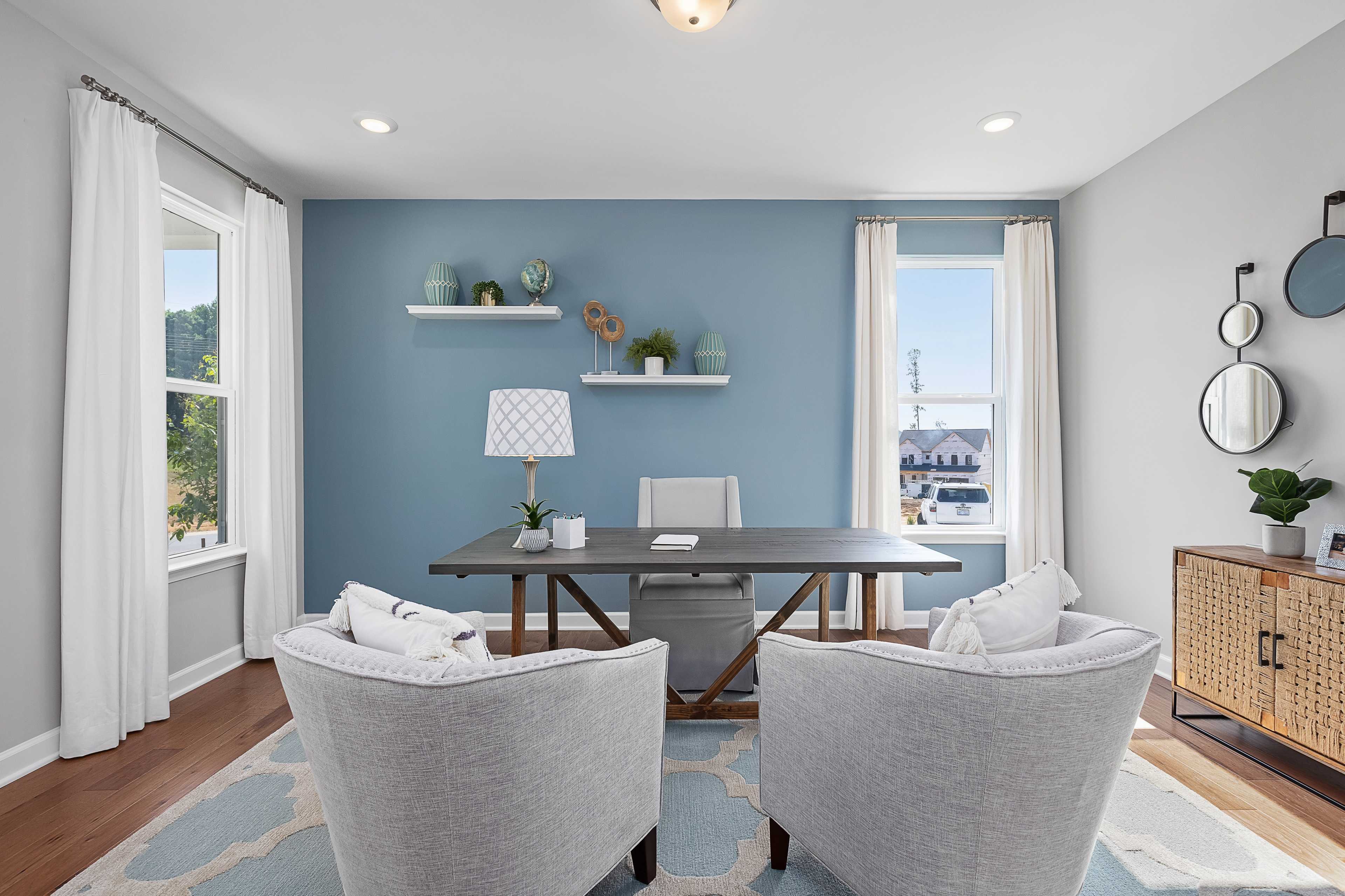 Modern home office at Woodland Crossing in Zebulon NC with blue accent wall, wooden desk, armchairs, and natural light