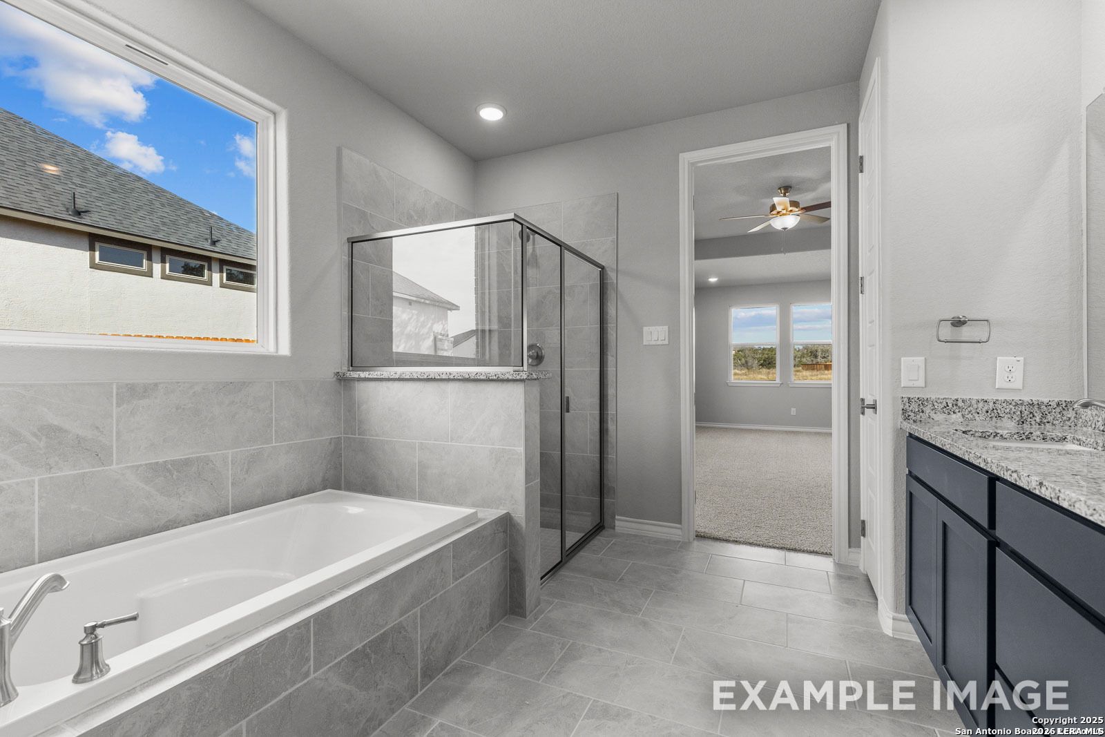 Modern primary bathroom with soaking tub, glass-enclosed shower, and granite vanity in The Oxford F at Potranco Oaks.