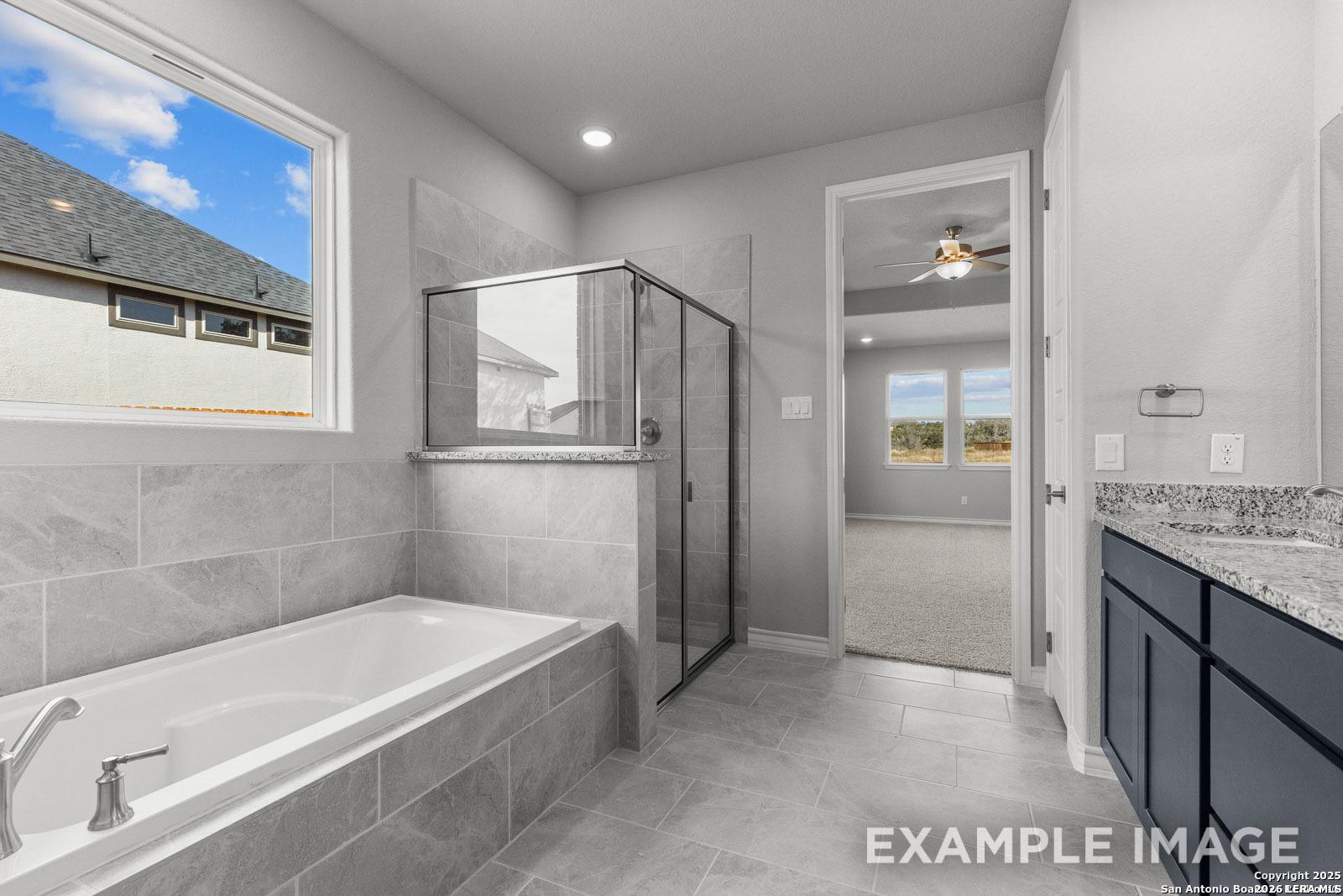 Modern primary bathroom with soaking tub, glass-enclosed shower, and granite vanity in The Oxford F at Potranco Oaks.
