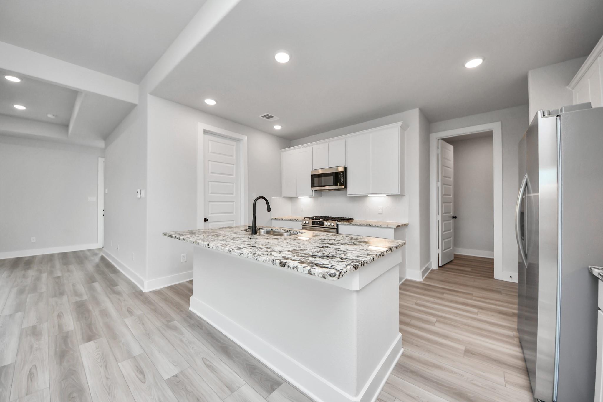 Modern kitchen with granite island and white cabinets in The Laguna C floor plan by Davidson Homes in Sunterra, Katy, Texas.