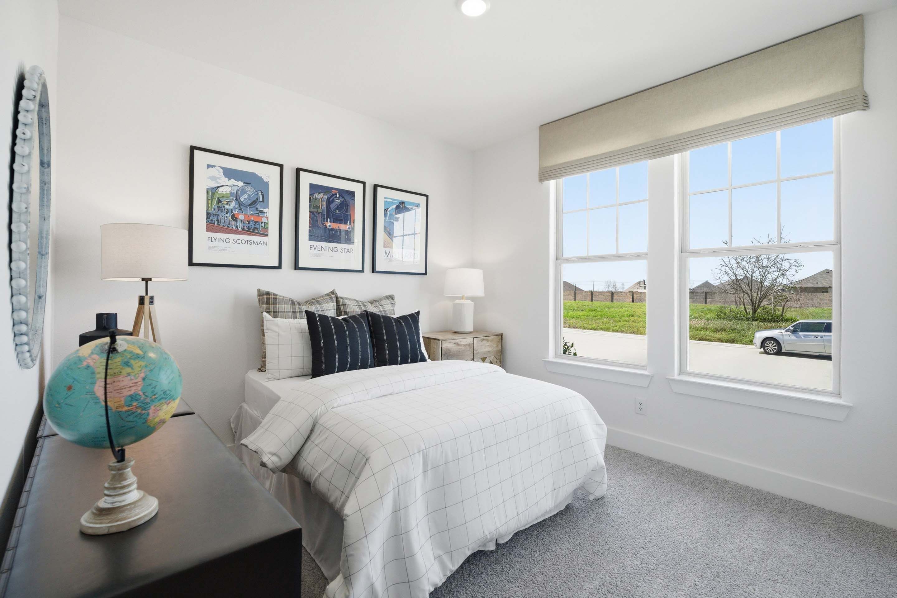 Bright secondary bedroom in The Laurel home design featuring a cozy bed, travel-themed decor, and large windows.